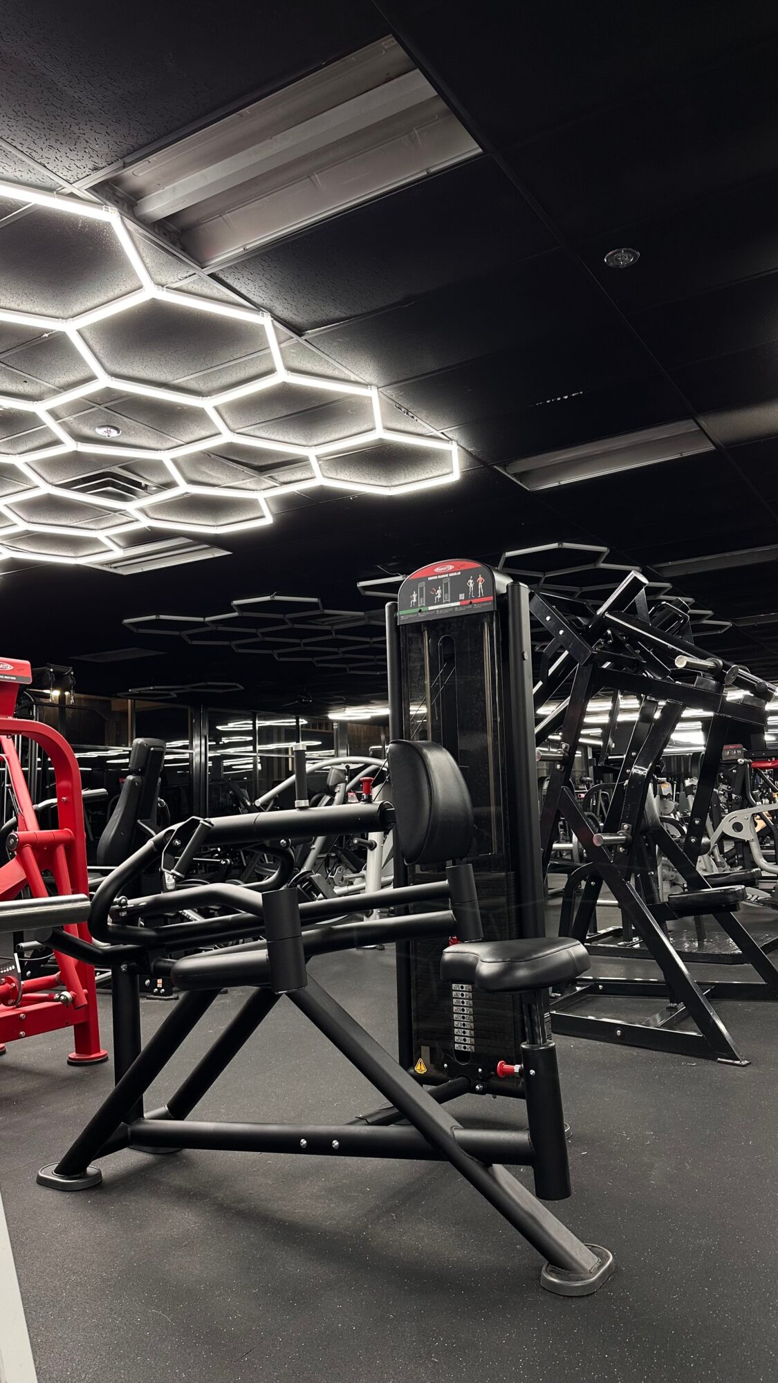 Gym with exercise equipment and hexagonal ceiling lights, black walls, and a mirror in the background.