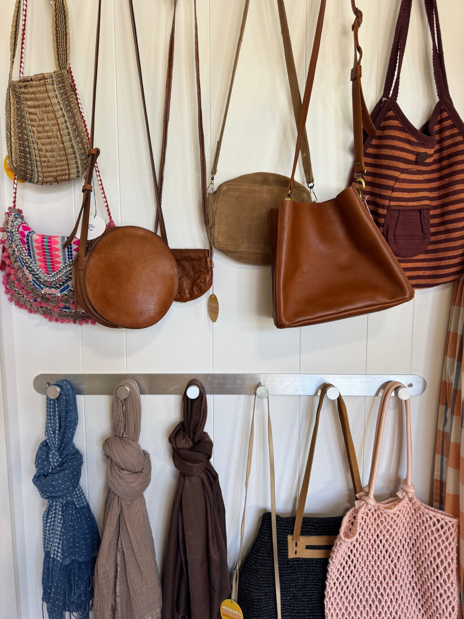 Display of handbags and scarves hanging on a wall, with various colors and textures.