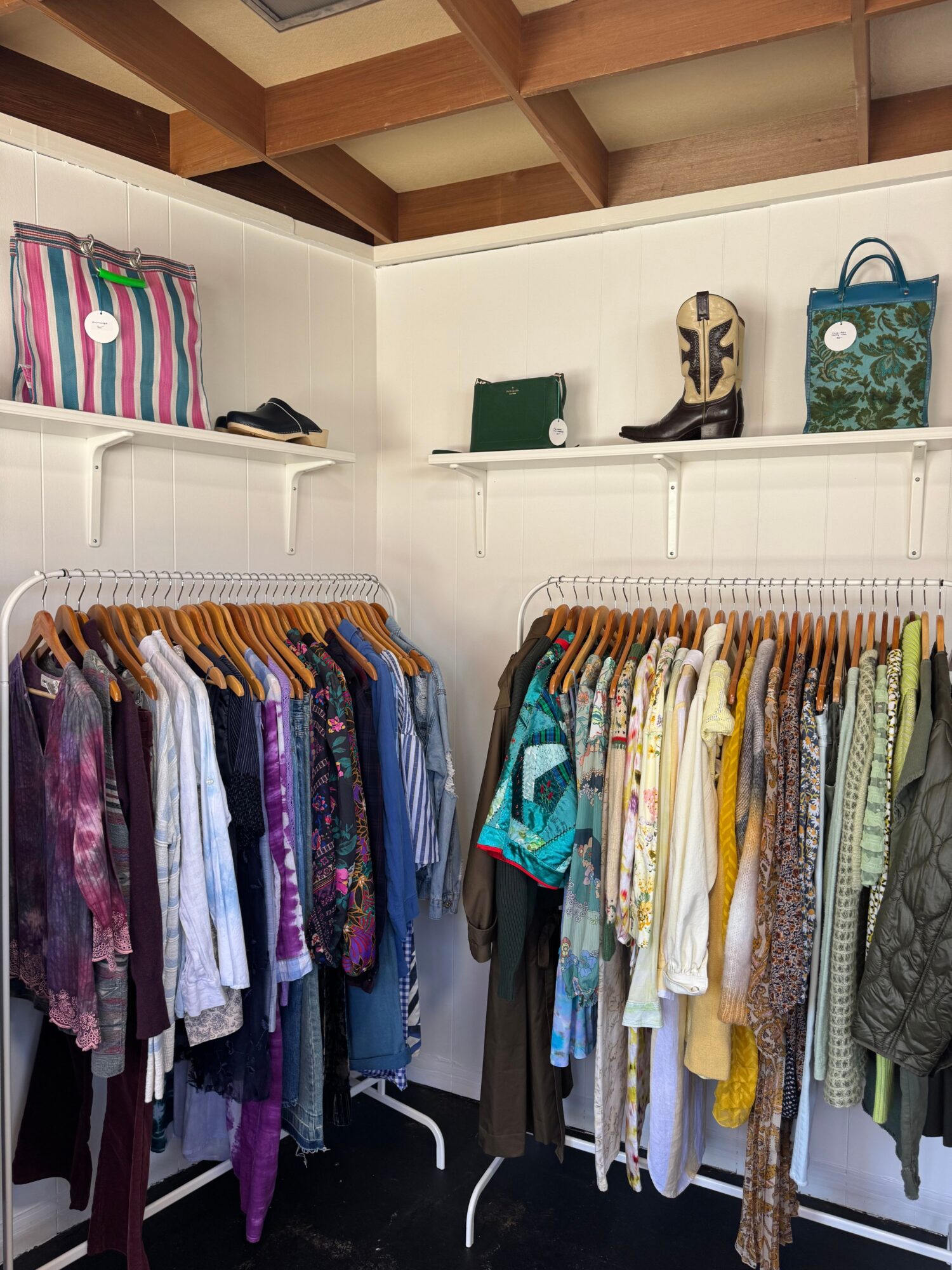 Clothes hanging on a rack with folded items and shelves in the background.