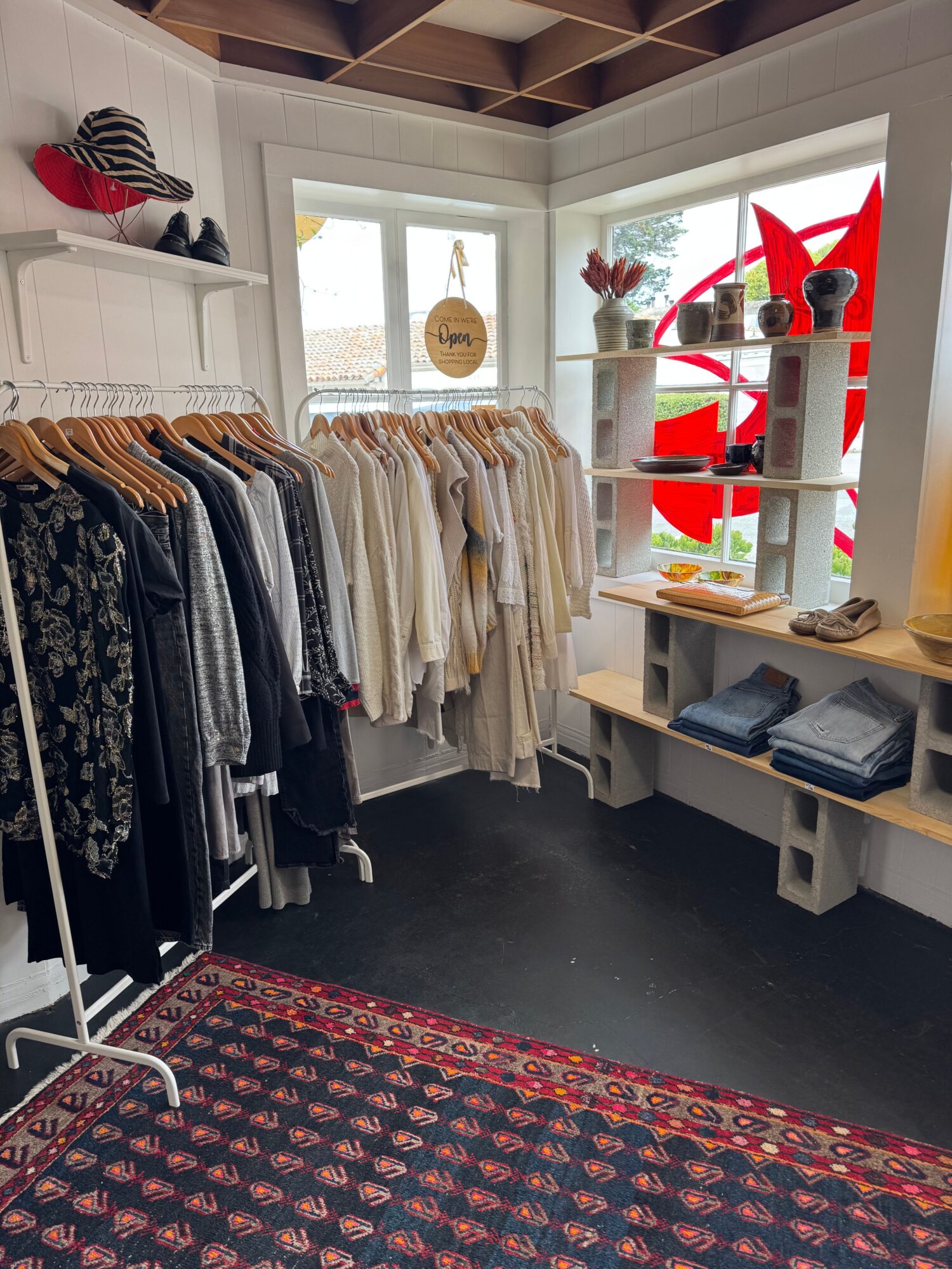 Clothing rack with hanging garments in a store, window with decorations and shelves in the background.