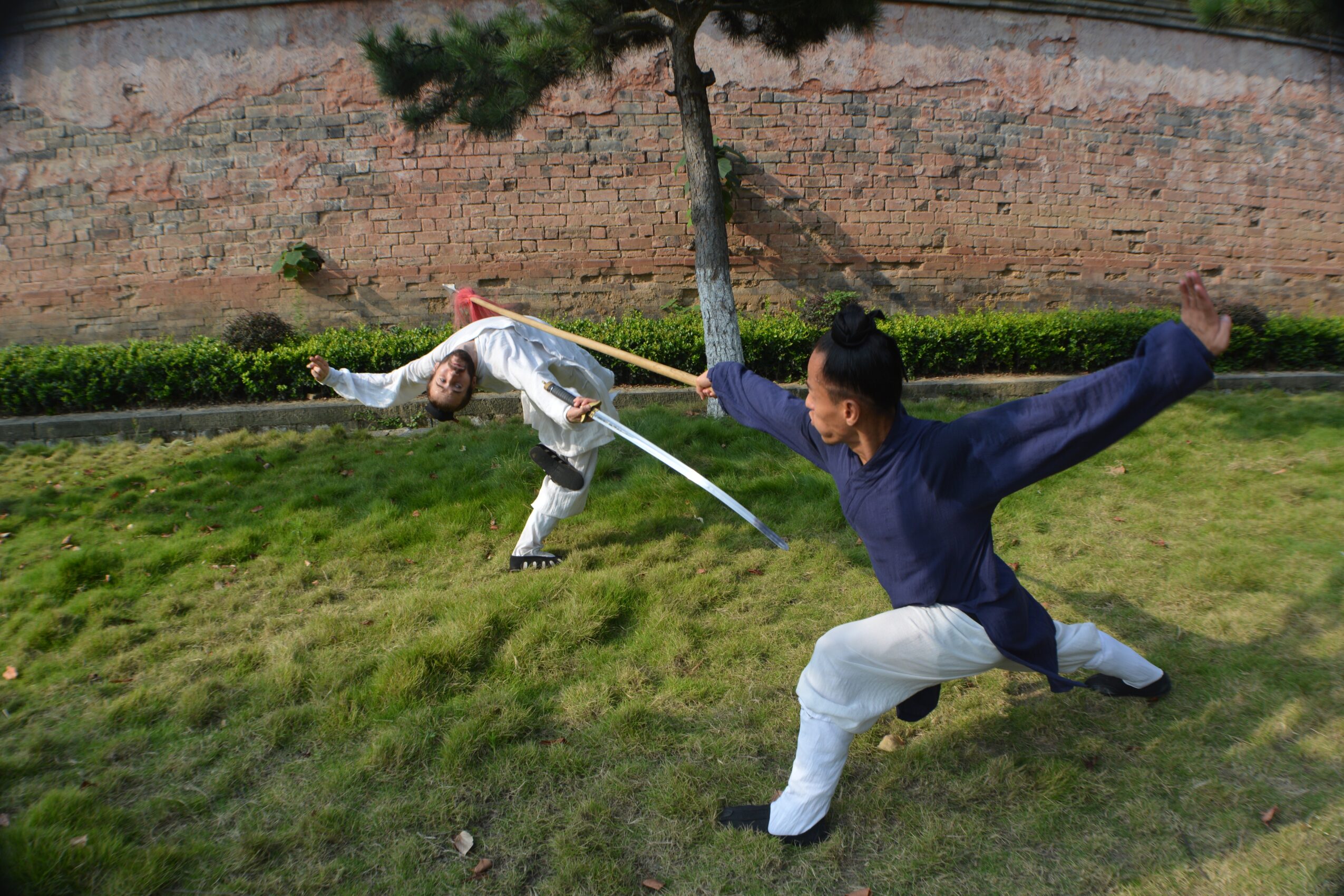 Two people practicing martial arts outdoors on grass, one in a defensive stance and the other in a striking pose.