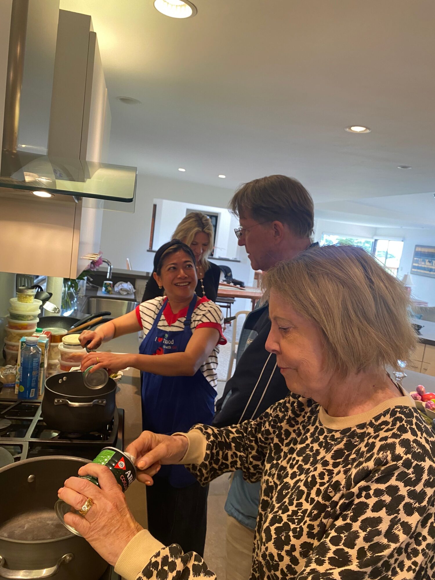 Three women in a kitchen, one cooking, others watching, with various kitchen items on the counter.