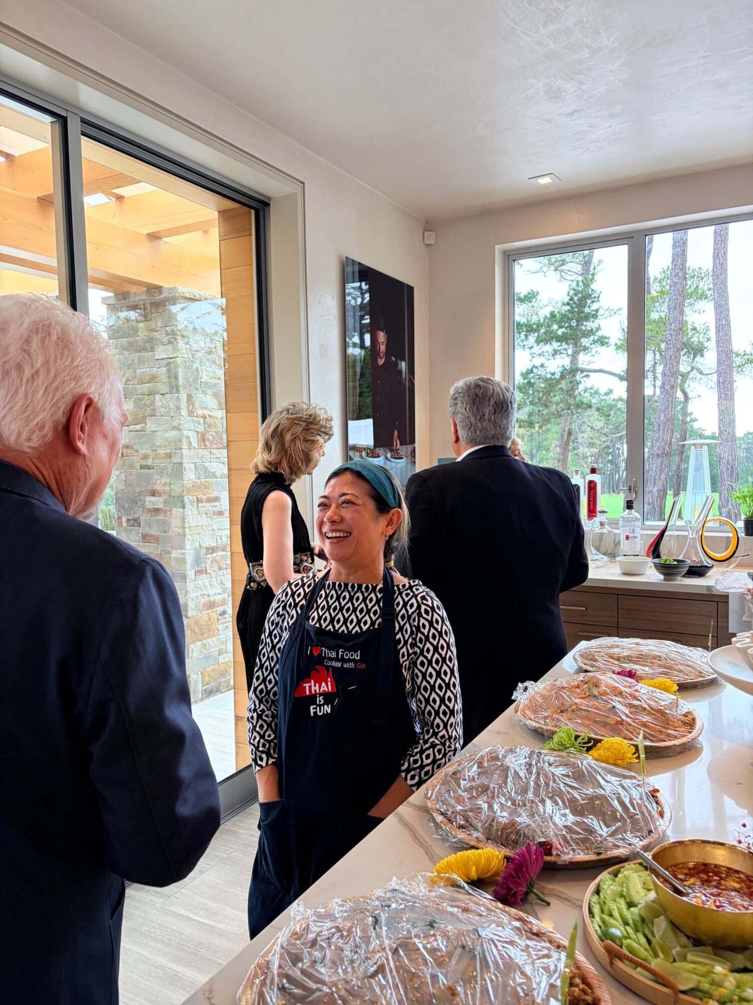 Two people standing near a table with wrapped food items, in a room with large windows and natural light.