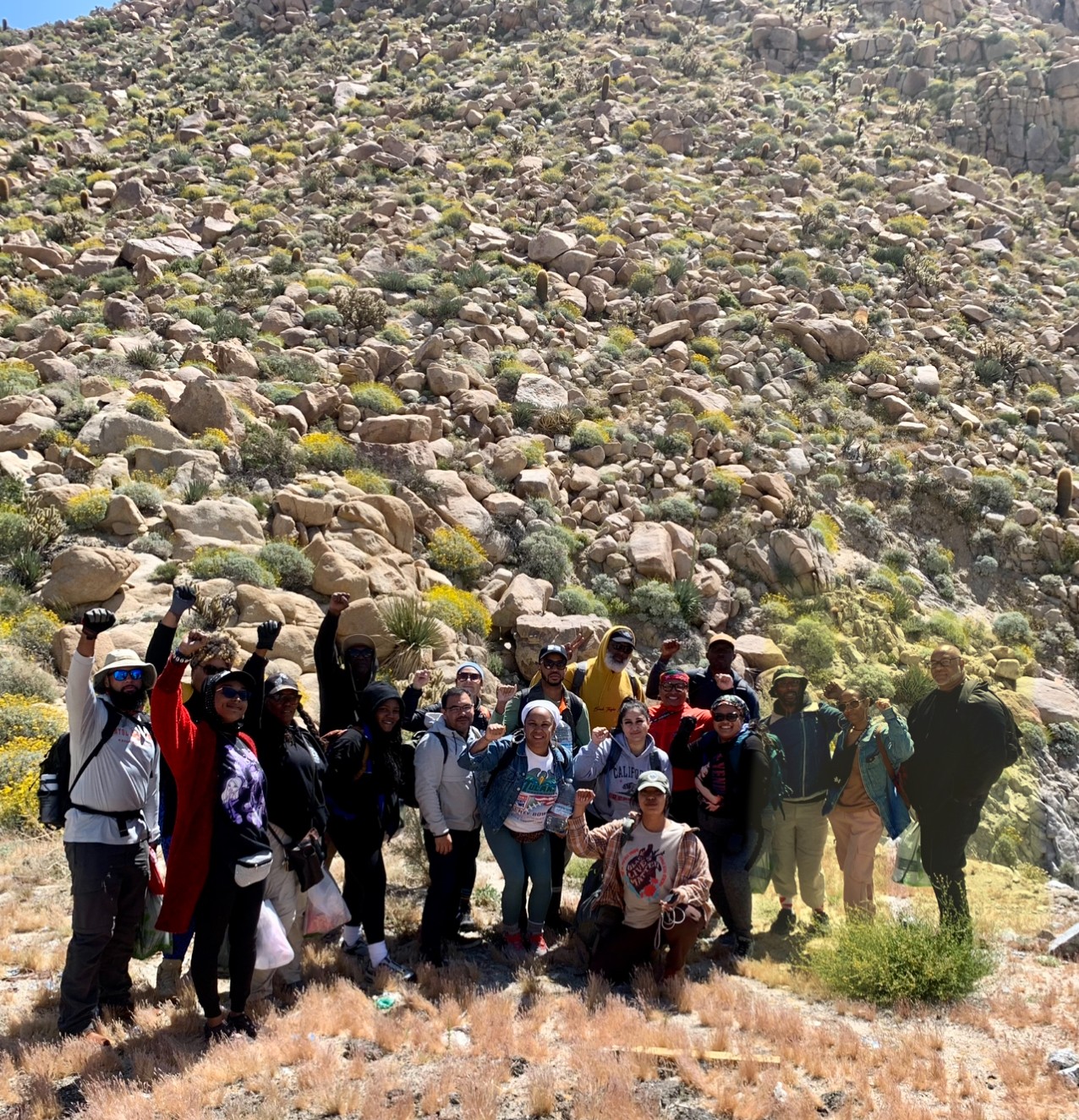 Group of people hiking on rocky terrain with a steep, rocky hillside in the background.