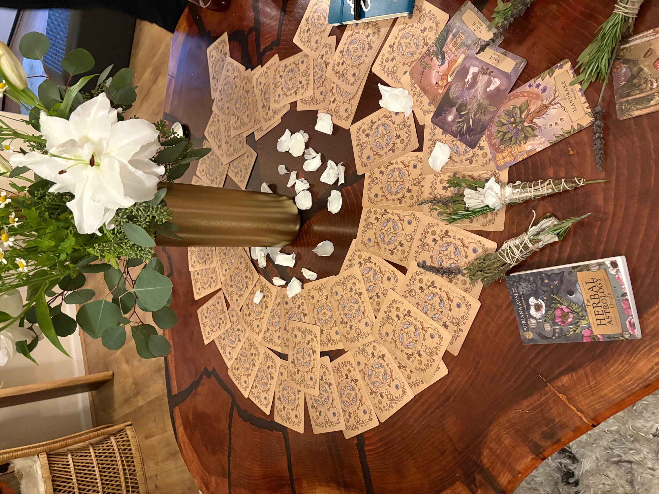 Table with tarot cards arranged in a semi-circle, white flowers in a gold vase, and scattered white stones.