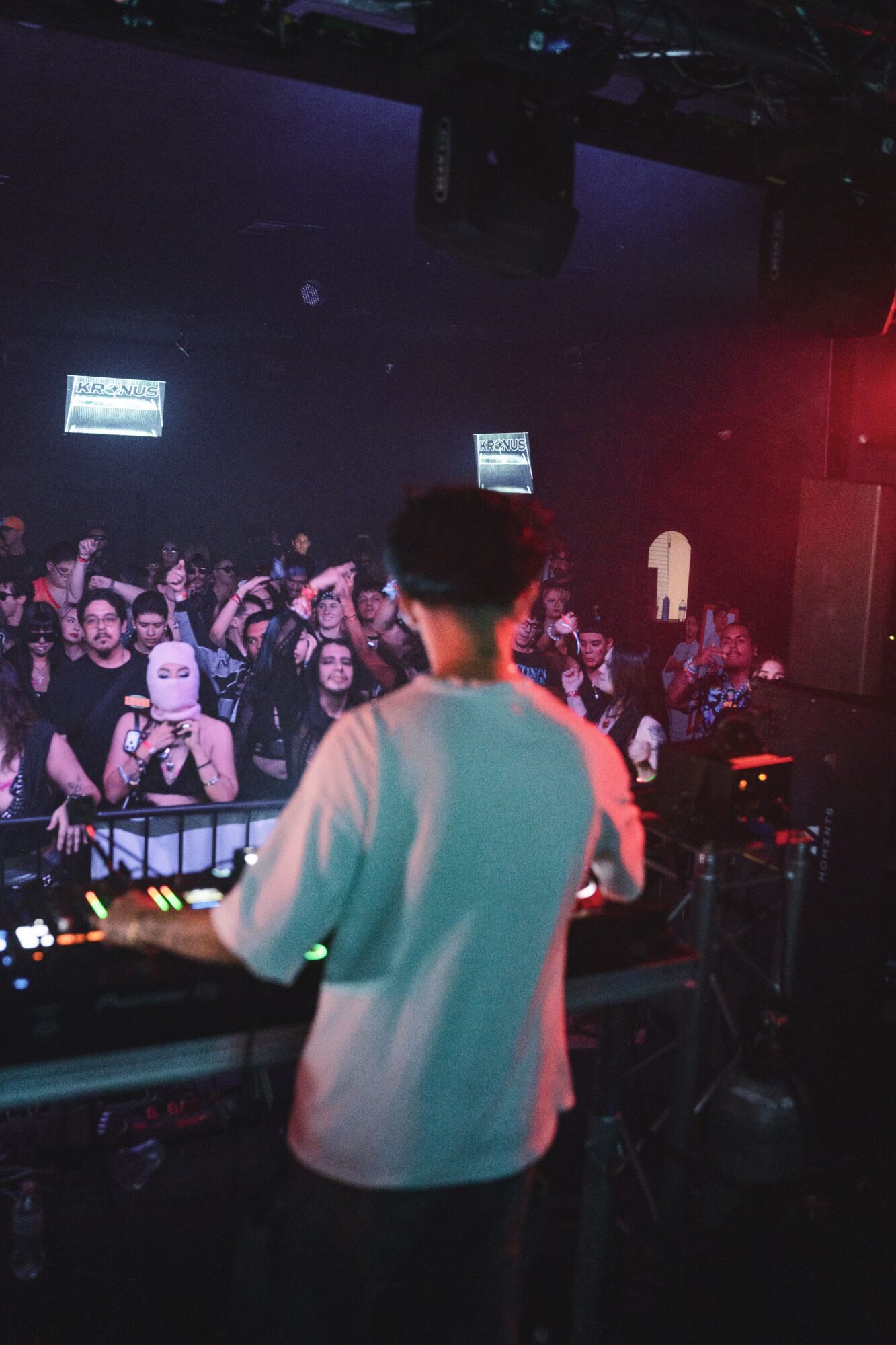 Person DJing at a crowded nightclub with colorful lighting and audience in the background.