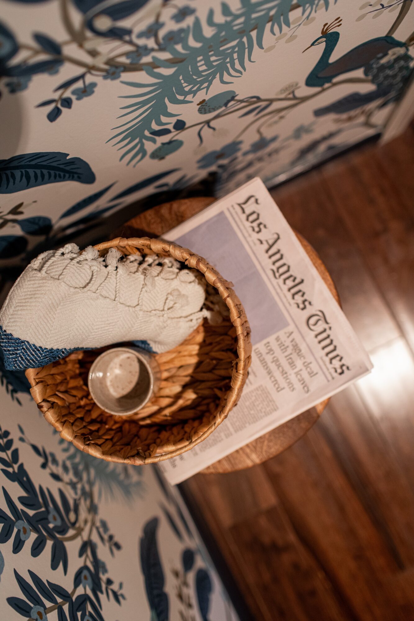 Basket with a sock, a small container, and a newspaper on a wooden surface, with a patterned fabric in the background.