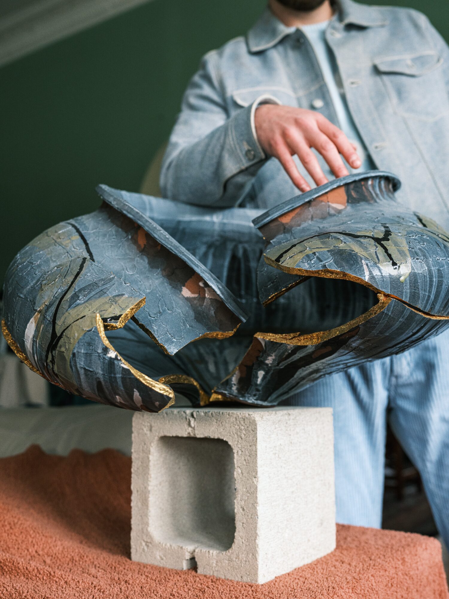 Person in denim jacket and jeans holding a torn balloon, with a green wall background.