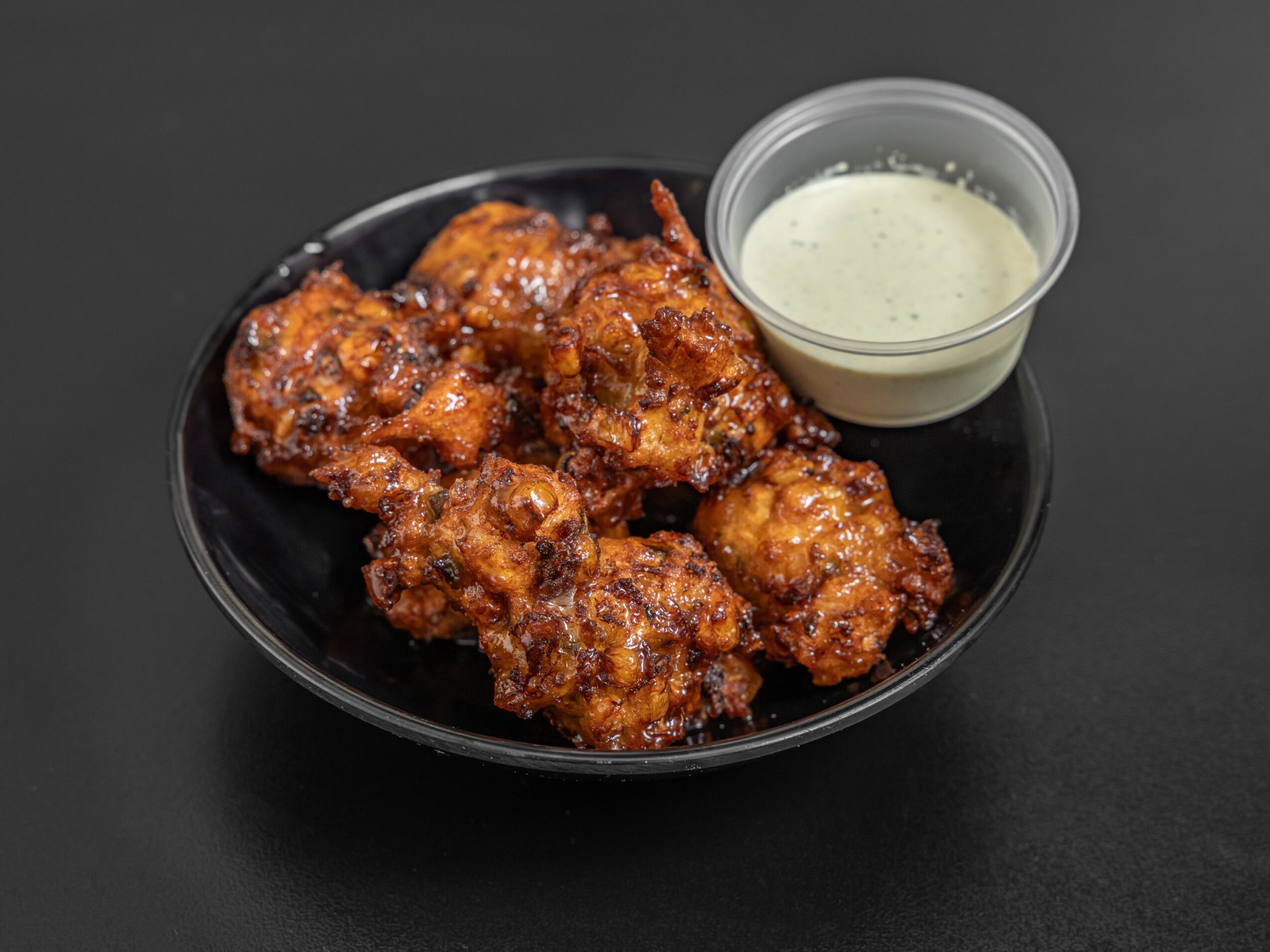 Fried chicken pieces with dipping sauce in a small container on a black plate, on a dark background.