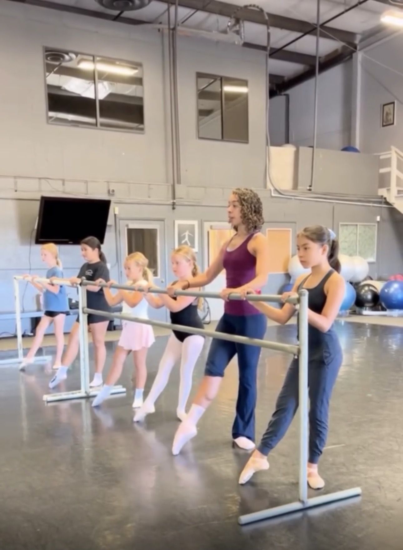 Group of children and an instructor practicing ballet at a dance studio with mirrors and ballet barres.