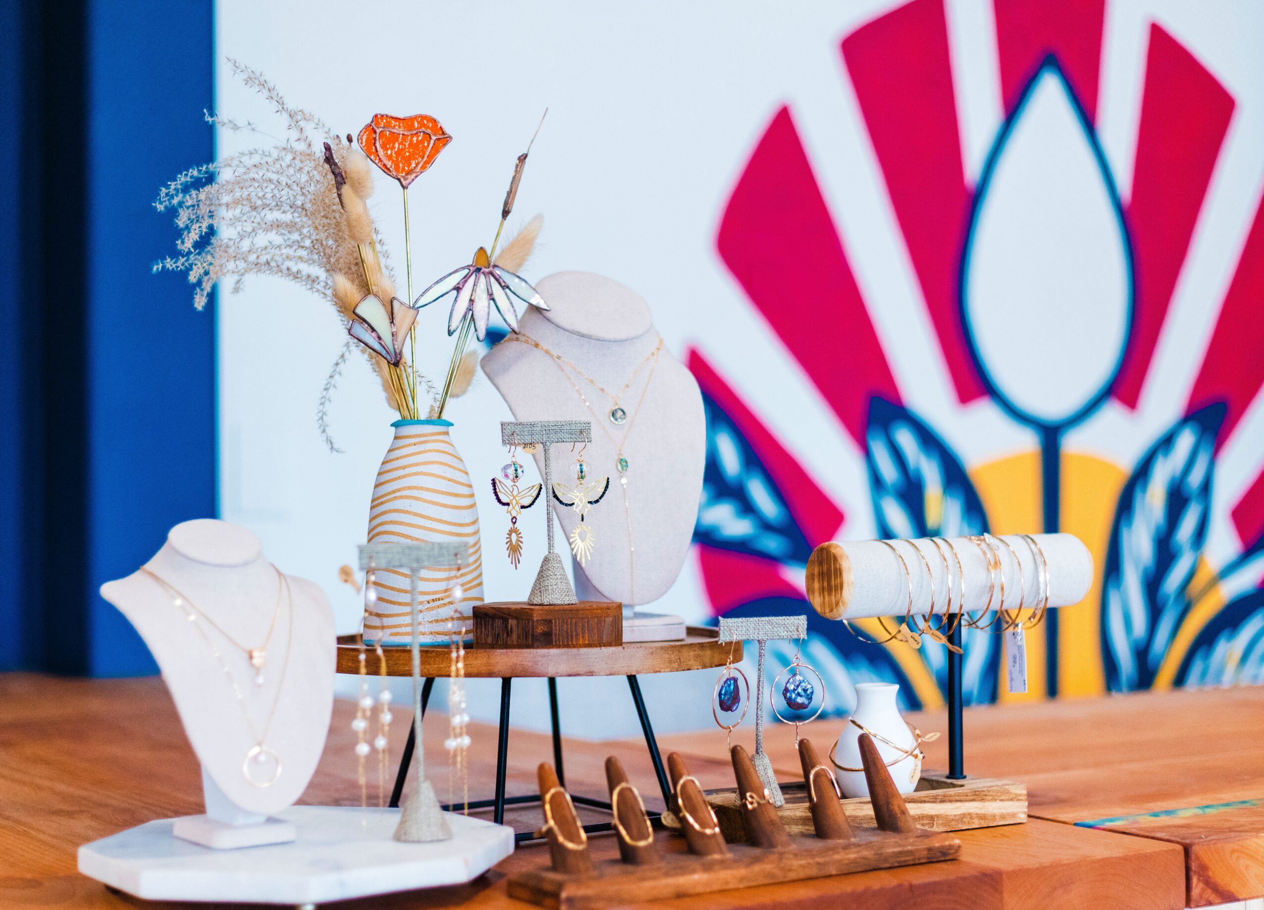 Display of jewelry and decorative items on a table with a colorful background, including necklaces, earrings, and a jewelry holder.