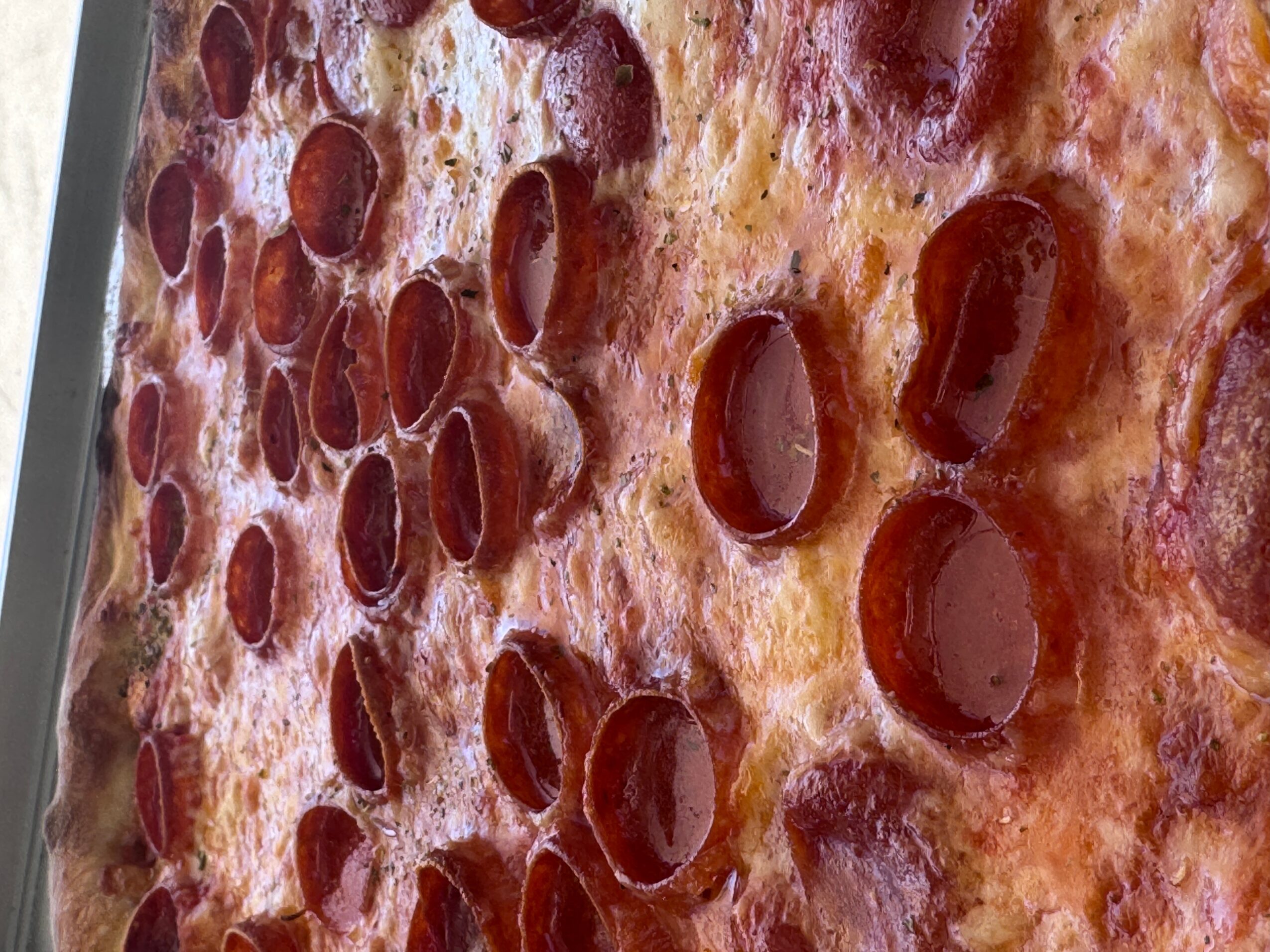 Close-up of a pepperoni pizza with melted cheese and pepperoni slices, viewed from the side.