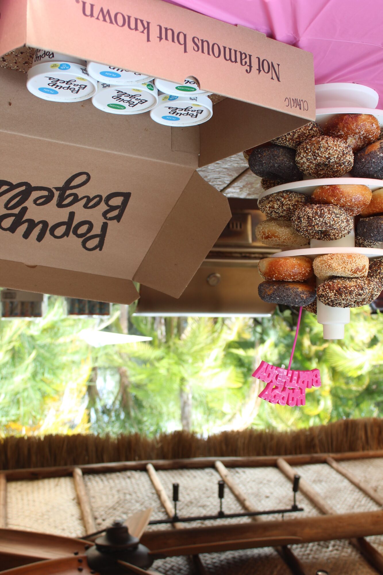 Table with assorted donuts, yogurt cups, and a cardboard box labeled 'Hoppy Bappy'. Bright outdoor setting with trees and a thatched roof.