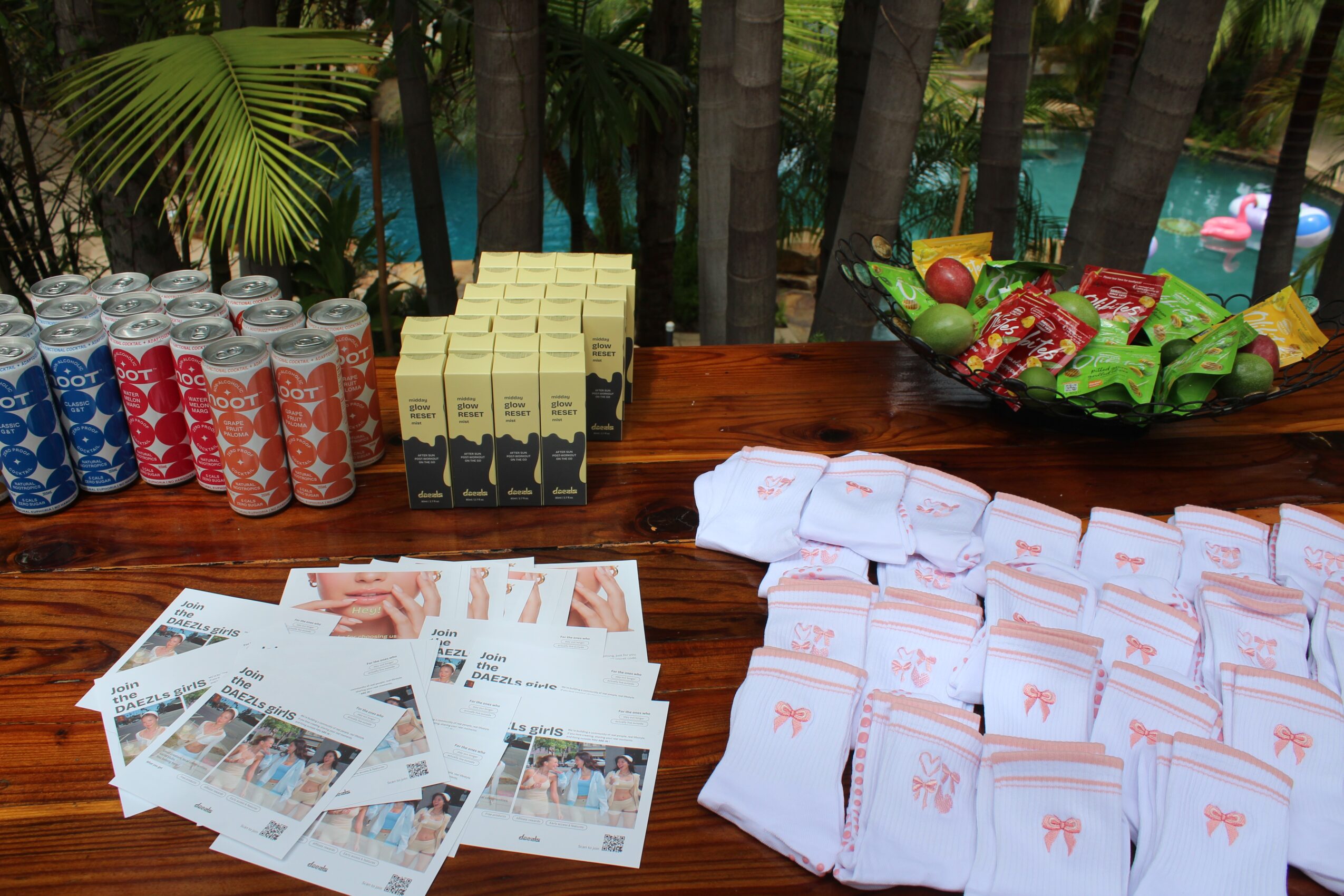 Table with drinks, snacks, and printed photos outdoors with trees and water in background.