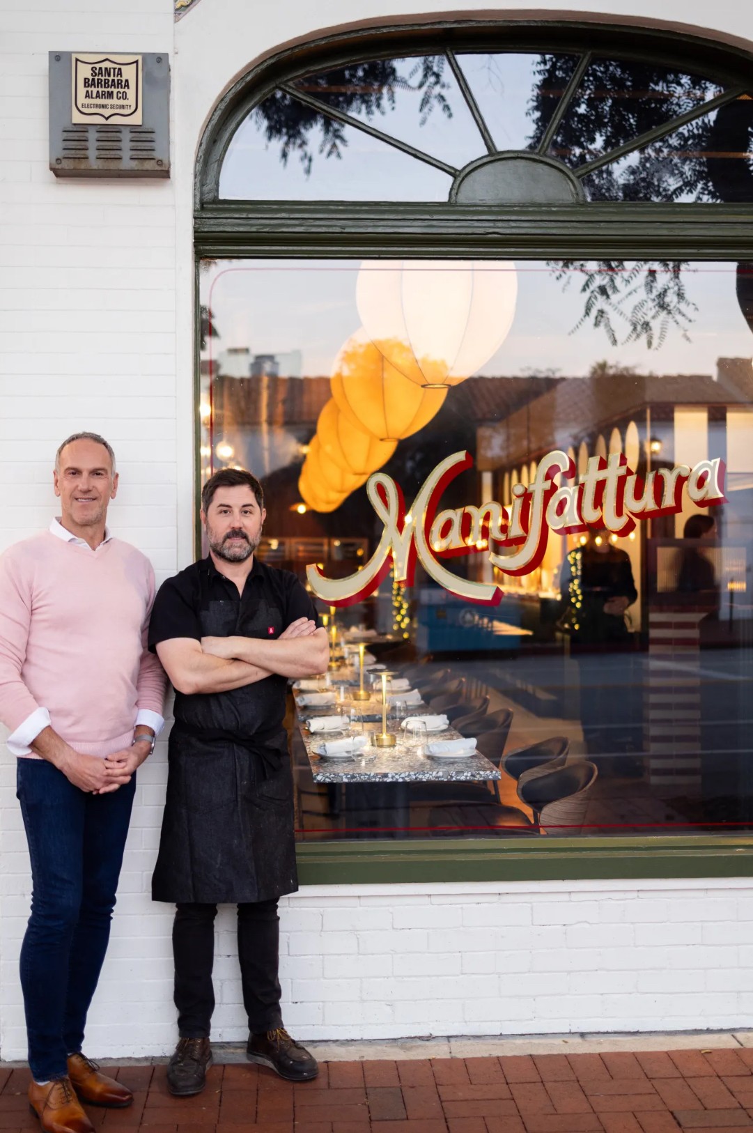 Two men stand outside a restaurant window with a display of food and a sign reading 'Maturattura'.
