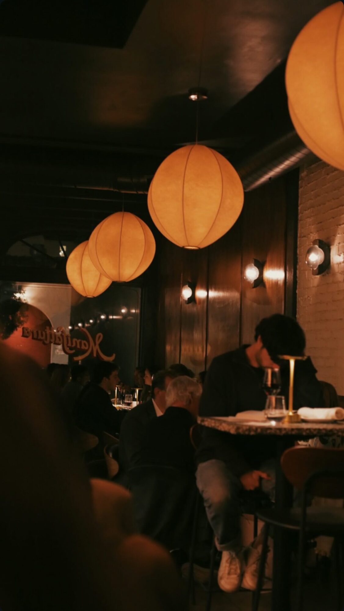 Interior of a restaurant with hanging orange paper lanterns and people dining at tables.