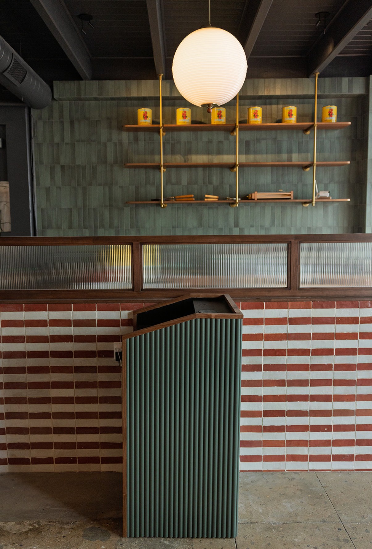 Interior with a hanging round light, shelves with yellow objects, and a green and black striped counter.