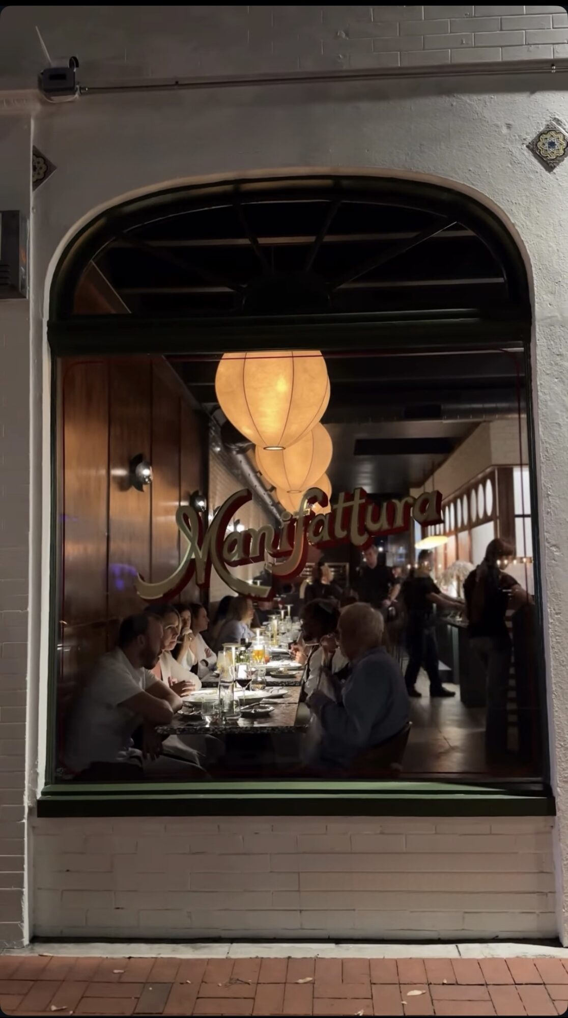Restaurant interior with hanging lanterns and people dining, viewed through a window with the word 'Augustus' on it.