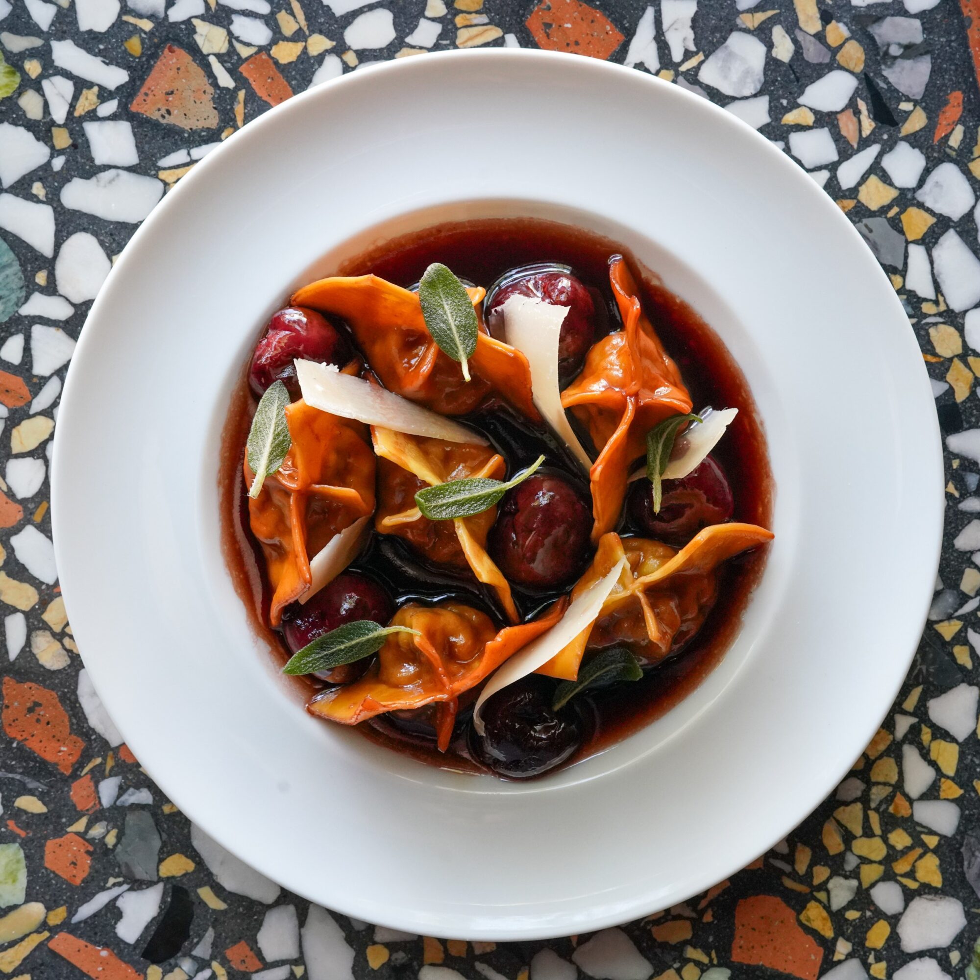 A bowl of pasta with sauce, garnished with herbs and vegetables, on a patterned surface.