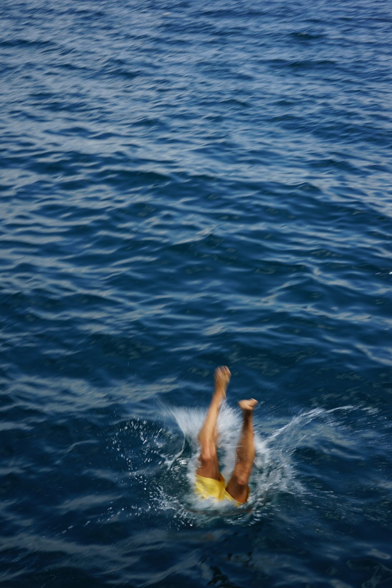 Person falling into water with legs and arms visible, surrounded by blue water, splashing around.
