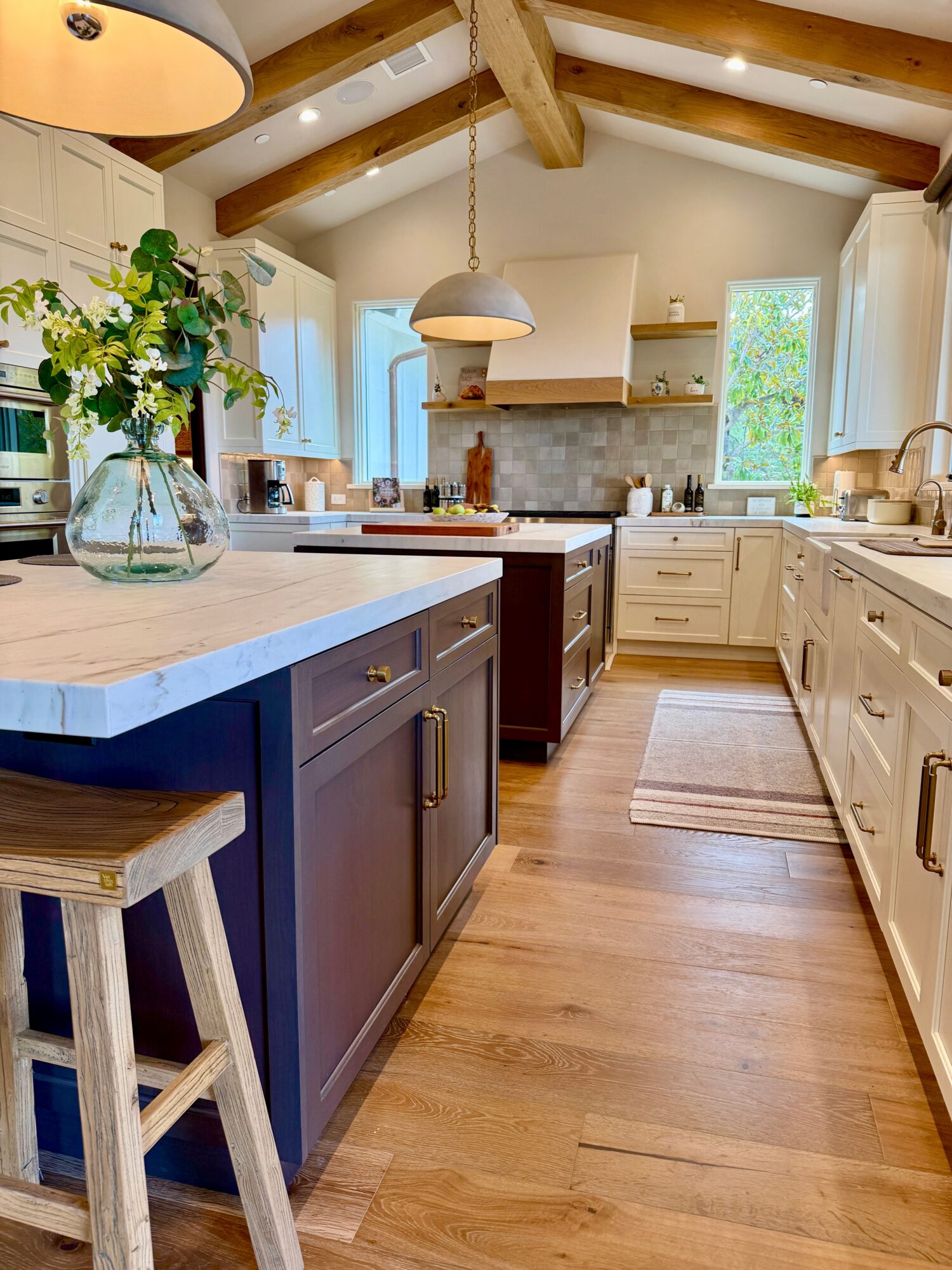 Kitchen with white cabinets, wooden beams, and a central island with a blue base, decorated with a vase of flowers.