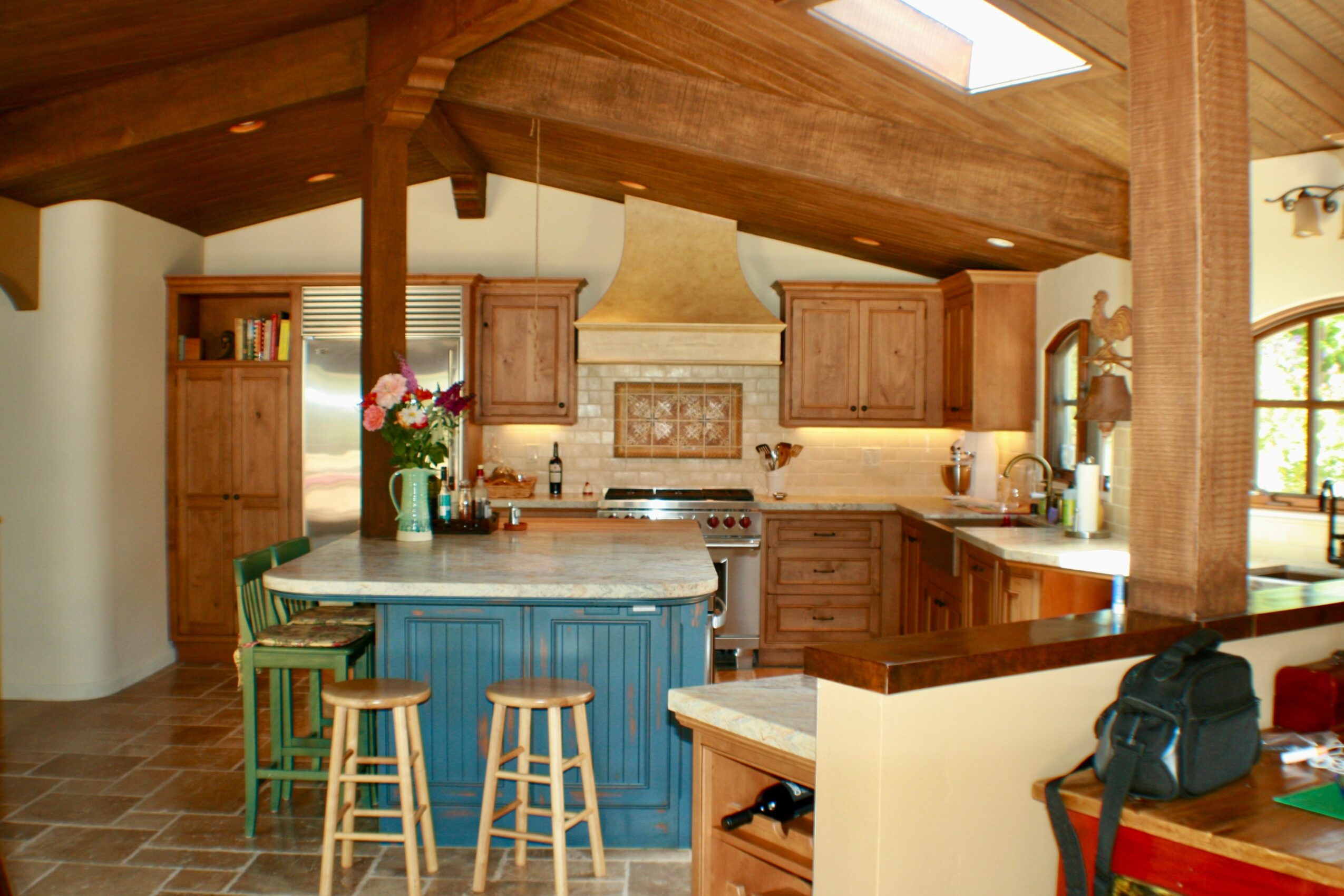Kitchen with wooden cabinets, a central island with stools, and a sloped wooden ceiling with skylight.