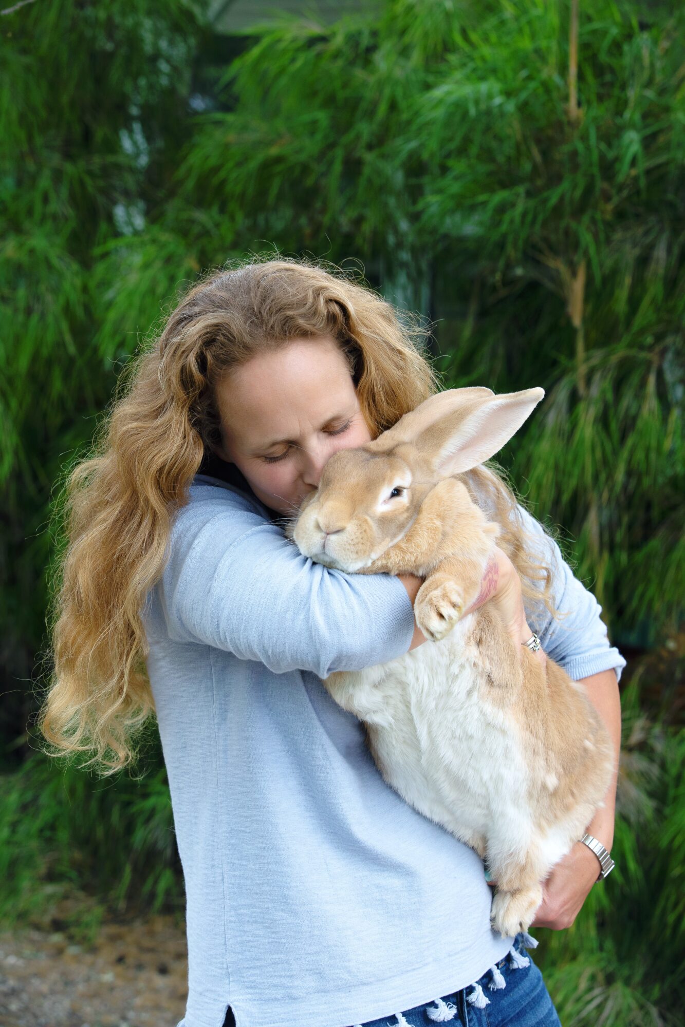 Woman hugging a large rabbit outdoors with green foliage in background.