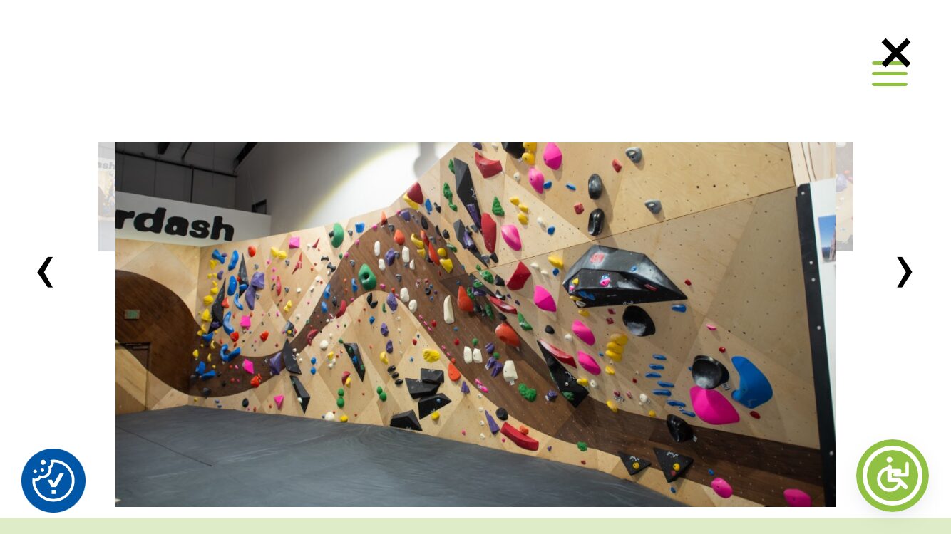 Indoor climbing wall with colorful holds and a black car-shaped climbing feature, beige background, and a gray floor.