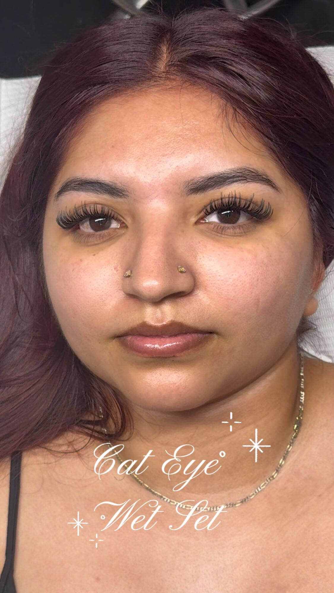 Close-up of a woman with makeup, nose piercings, and dark hair, looking at the camera.