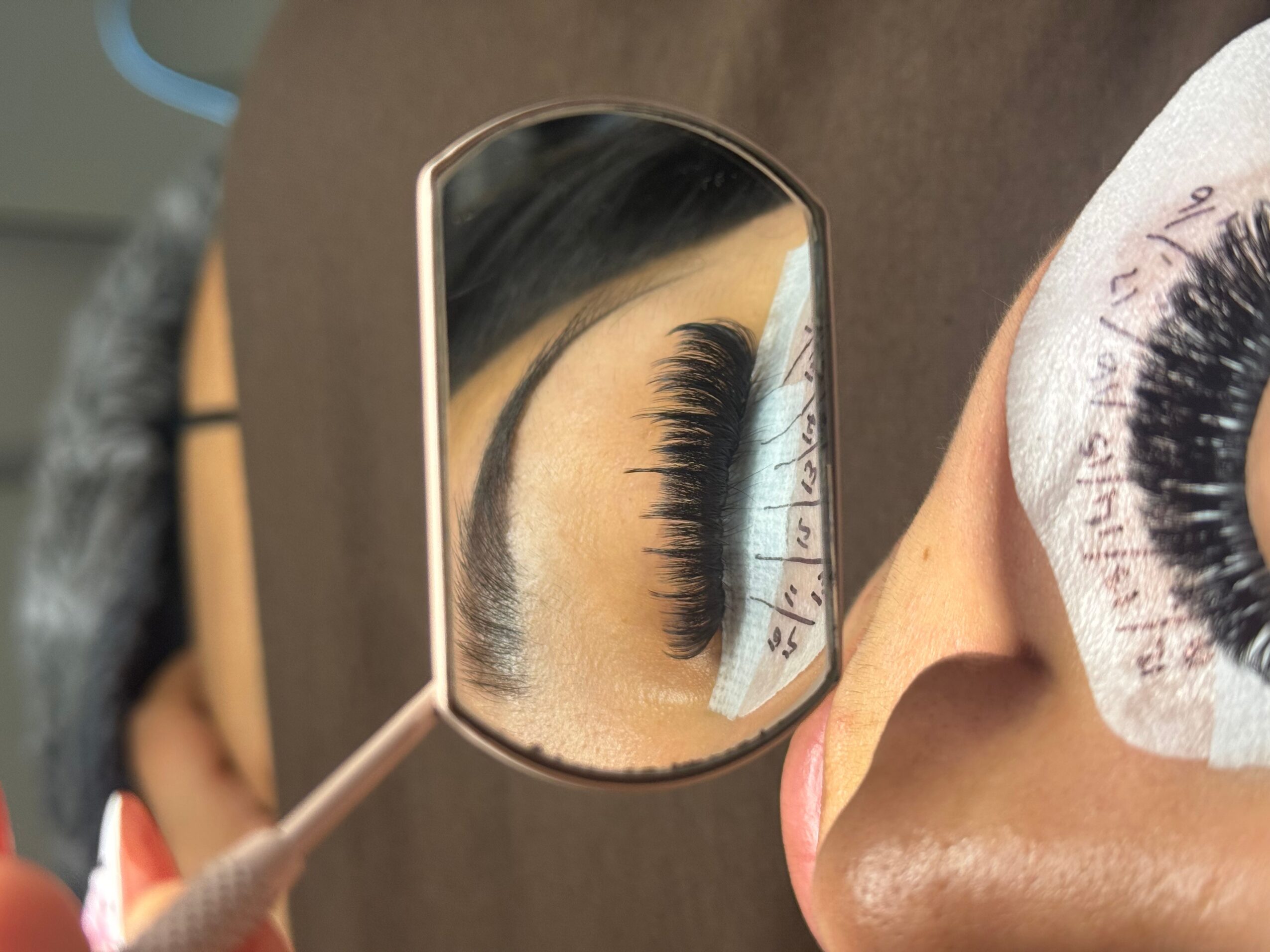 Person's eye with long eyelashes reflected in a small mirror, with makeup tools nearby.
