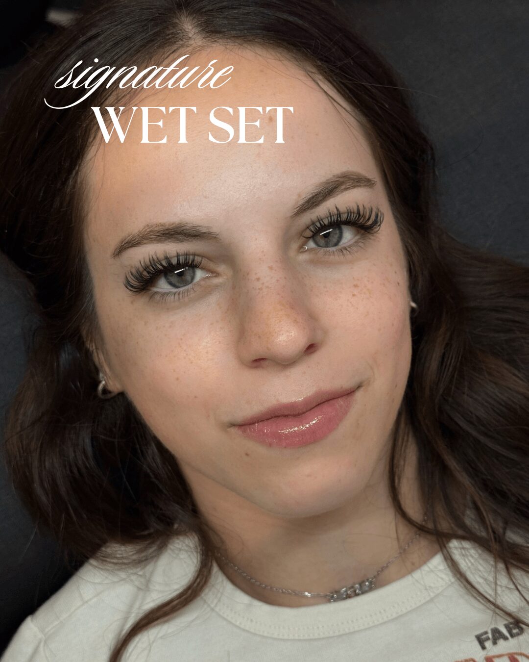 Close-up of a young woman with makeup, smiling, with text 'signature WET SET' on her forehead.