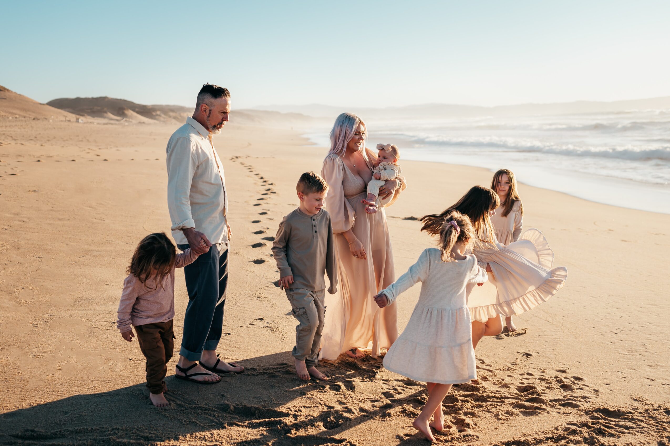 Group of children and adults walking on a sandy beach near the ocean, with waves and clear sky in the background.