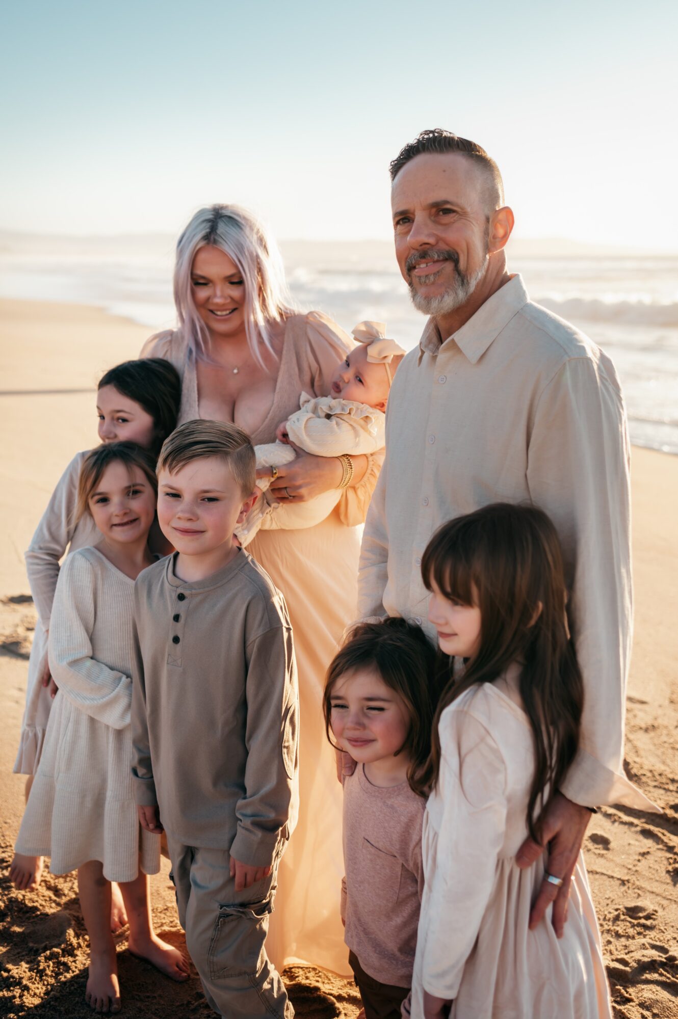 Family of seven on the beach, smiling, with ocean and sky in background.