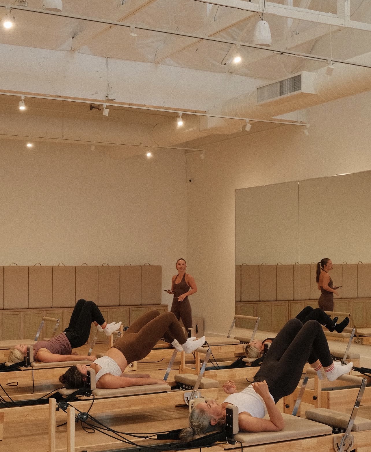 People practicing yoga or stretching on mats in a studio with wooden wall panels and ceiling lights.