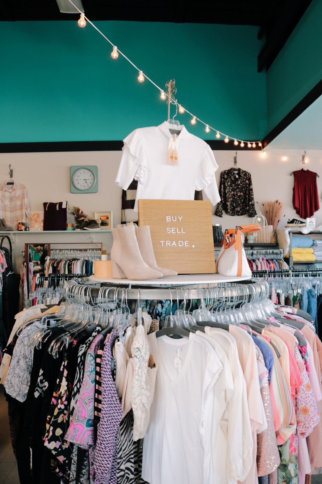 Clothing store interior with hanging shirts, shoes, and a sign reading 'Buy Sell Trade,' with racks of clothes and accessories.
