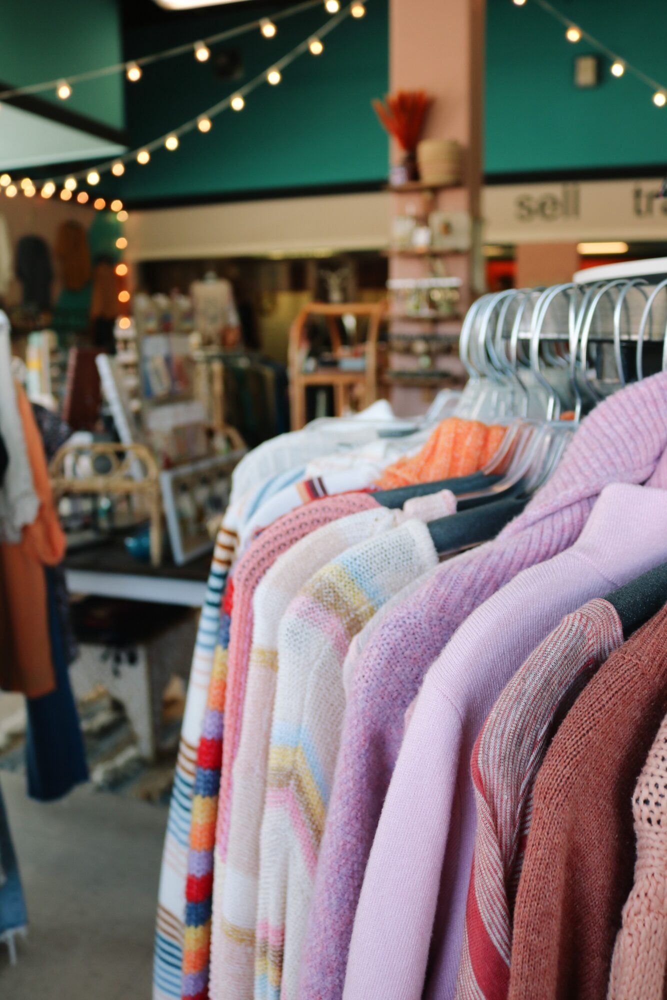 Clothing rack with colorful sweaters and shirts inside a store, with shelves and store signage in the background.