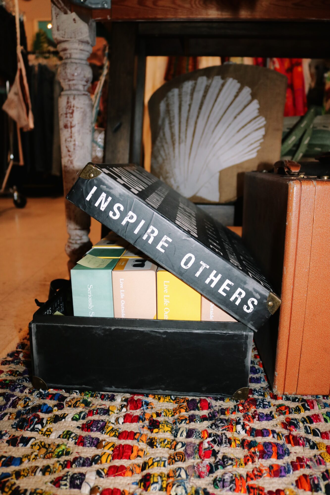 Books and a box on a colorful patterned rug with a shell decoration and furniture in the background.