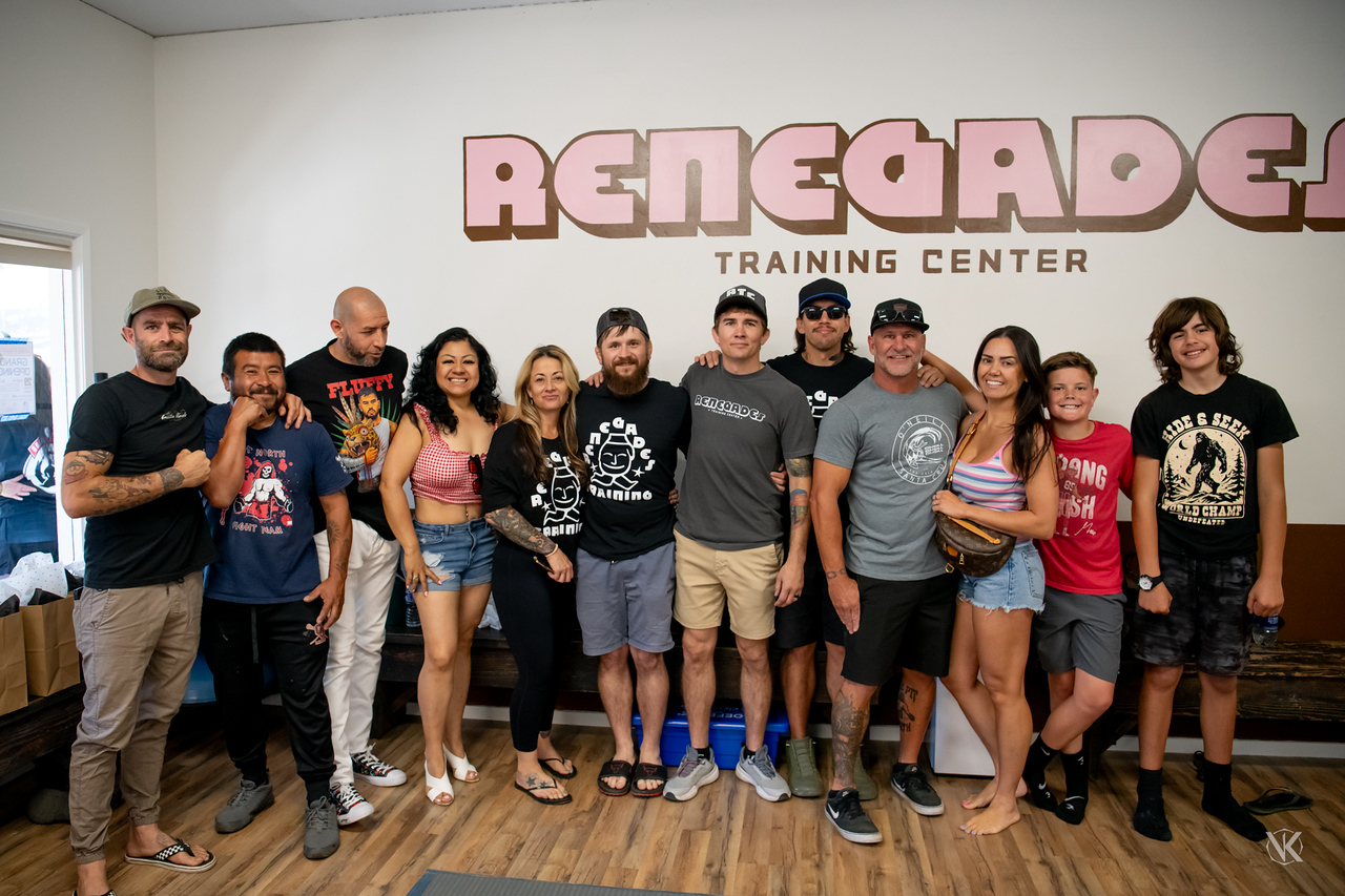 Group of people standing indoors in front of a wall with a sign that reads 'RENEGADE TRAINING CENTER'.