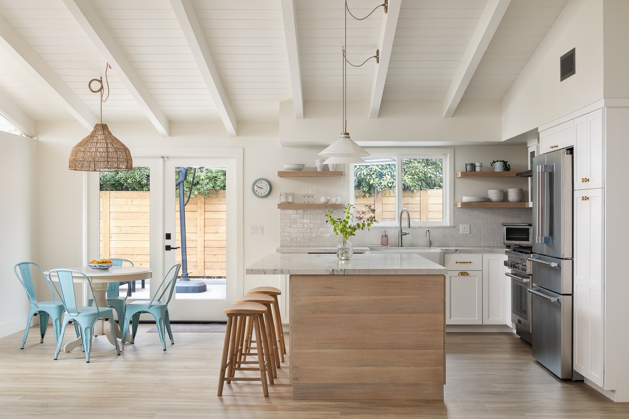 Bright kitchen and dining area with white walls, wooden accents, and large windows, featuring a dining table with chairs and a kitchen island.