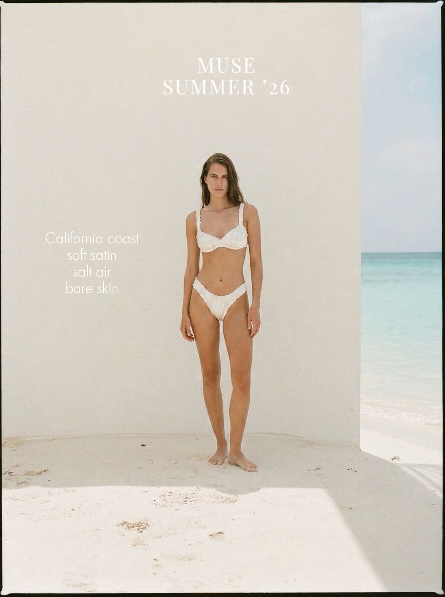 Woman in white bikini standing on beach with ocean background, white wall behind her, sunlight casting shadows.