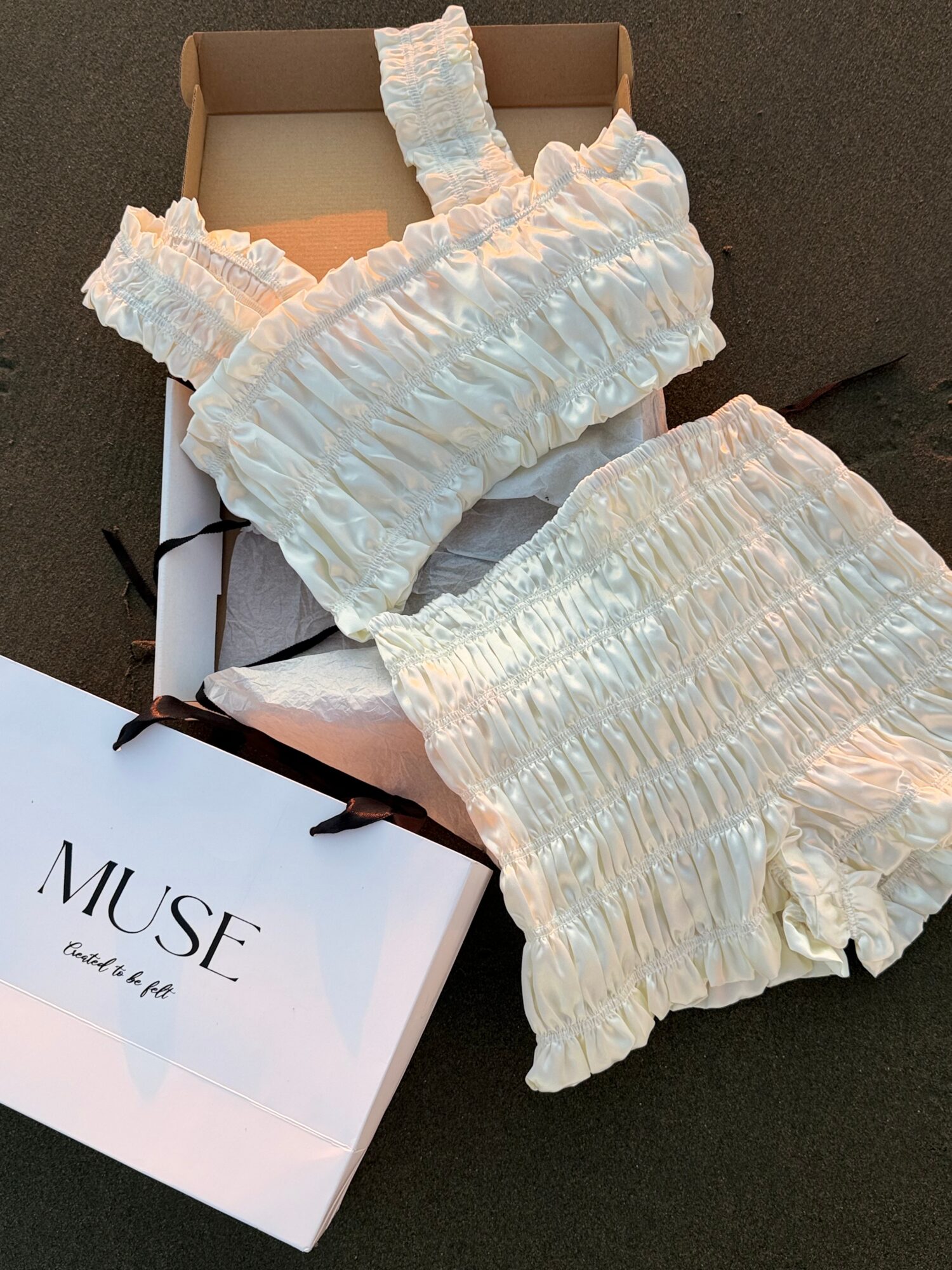 White ruffled clothing set on a box, with a shopping bag nearby, on a dark surface.