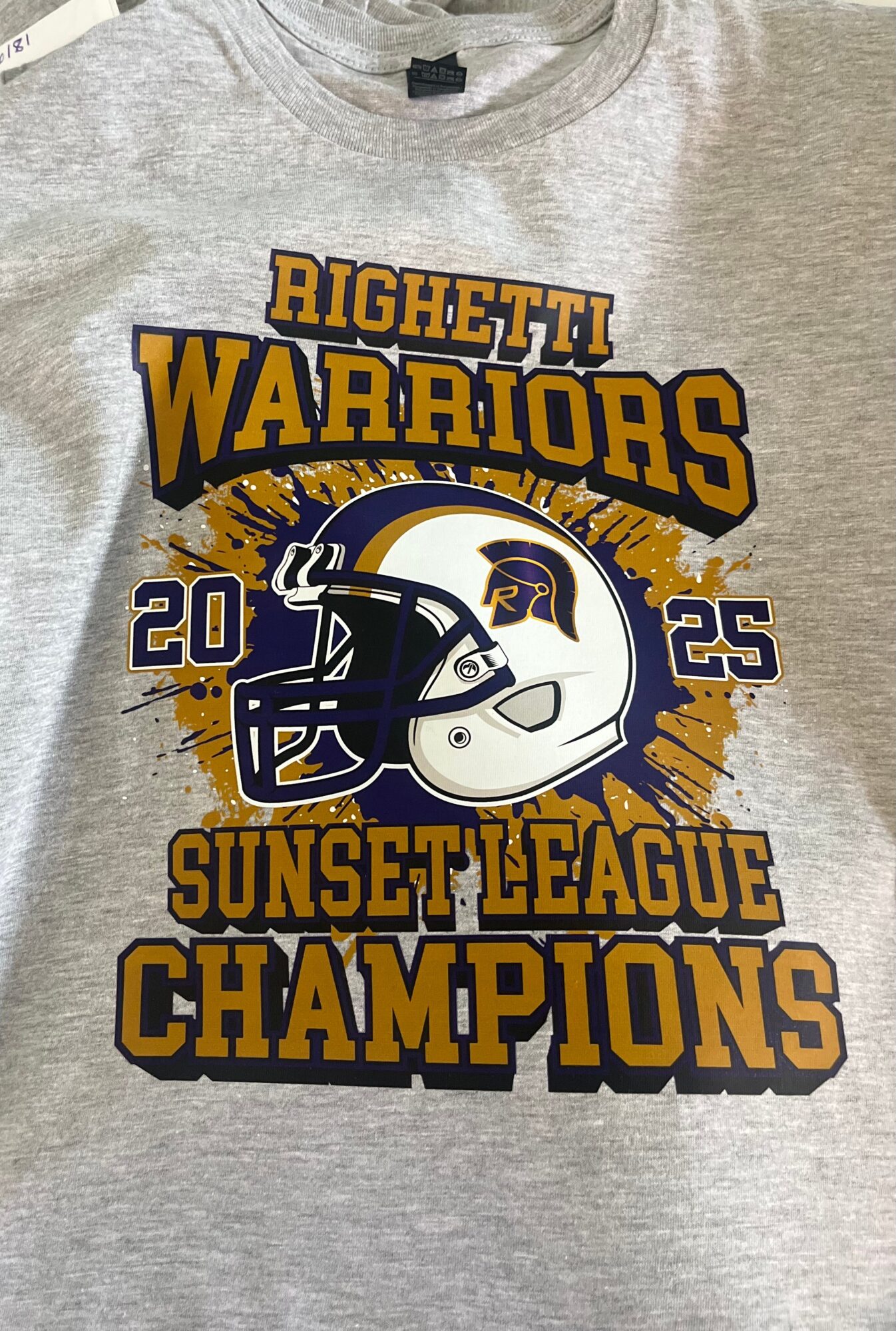 Gray T-shirt with a graphic celebrating Righetti Warriors' 2025 Sunset League Championship, featuring a football helmet and bold text.