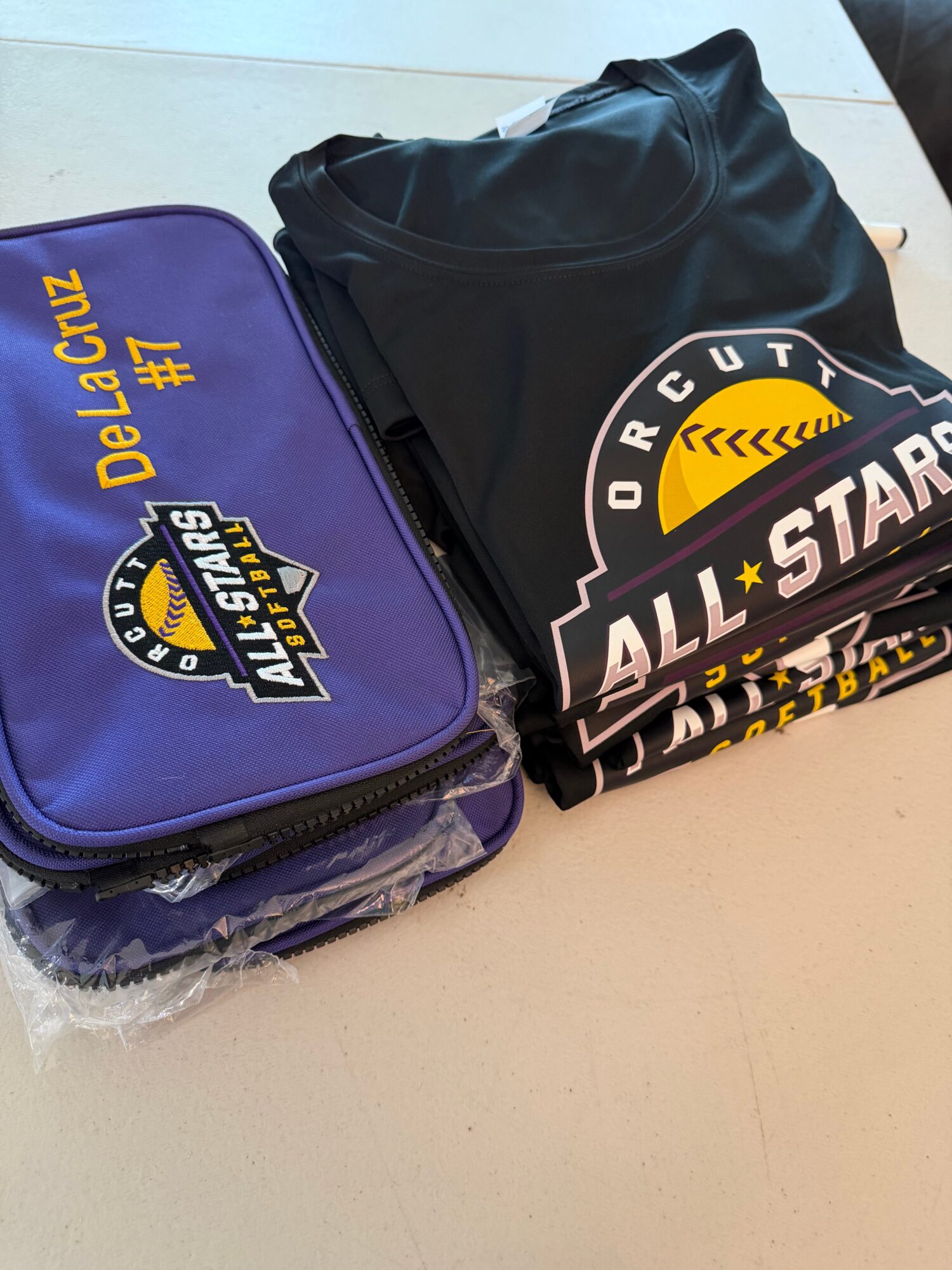 Black sports bag and purple bag with yellow and white text and logos on a light surface.