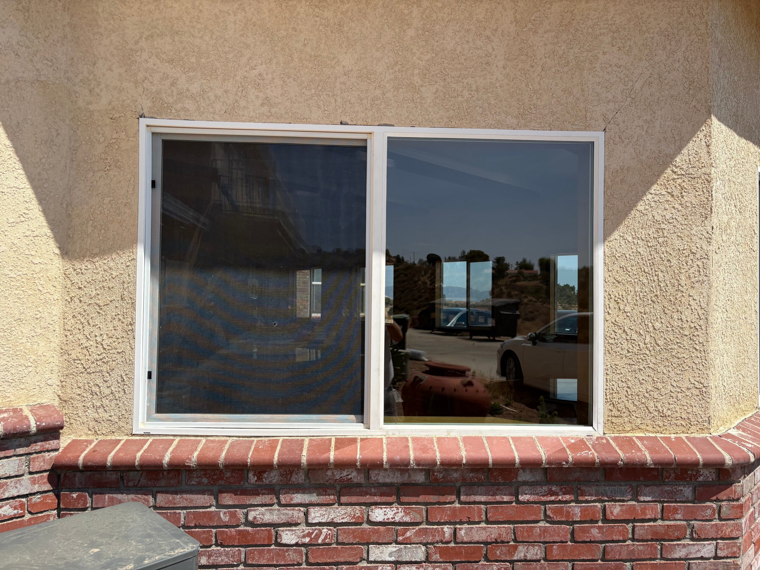 A window with two panes on a beige stucco wall, reflecting cars and trees outside.