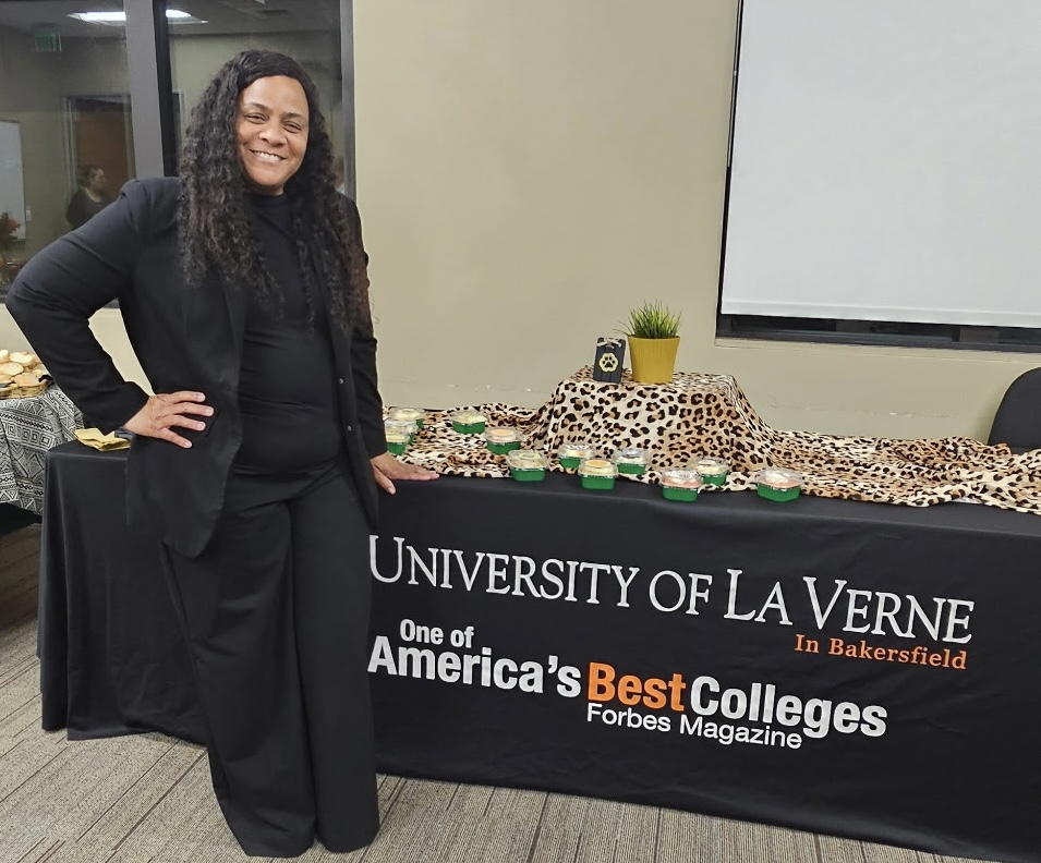 Woman in black suit standing next to a table with a leopard print cloth and a sign for University of La Verne.