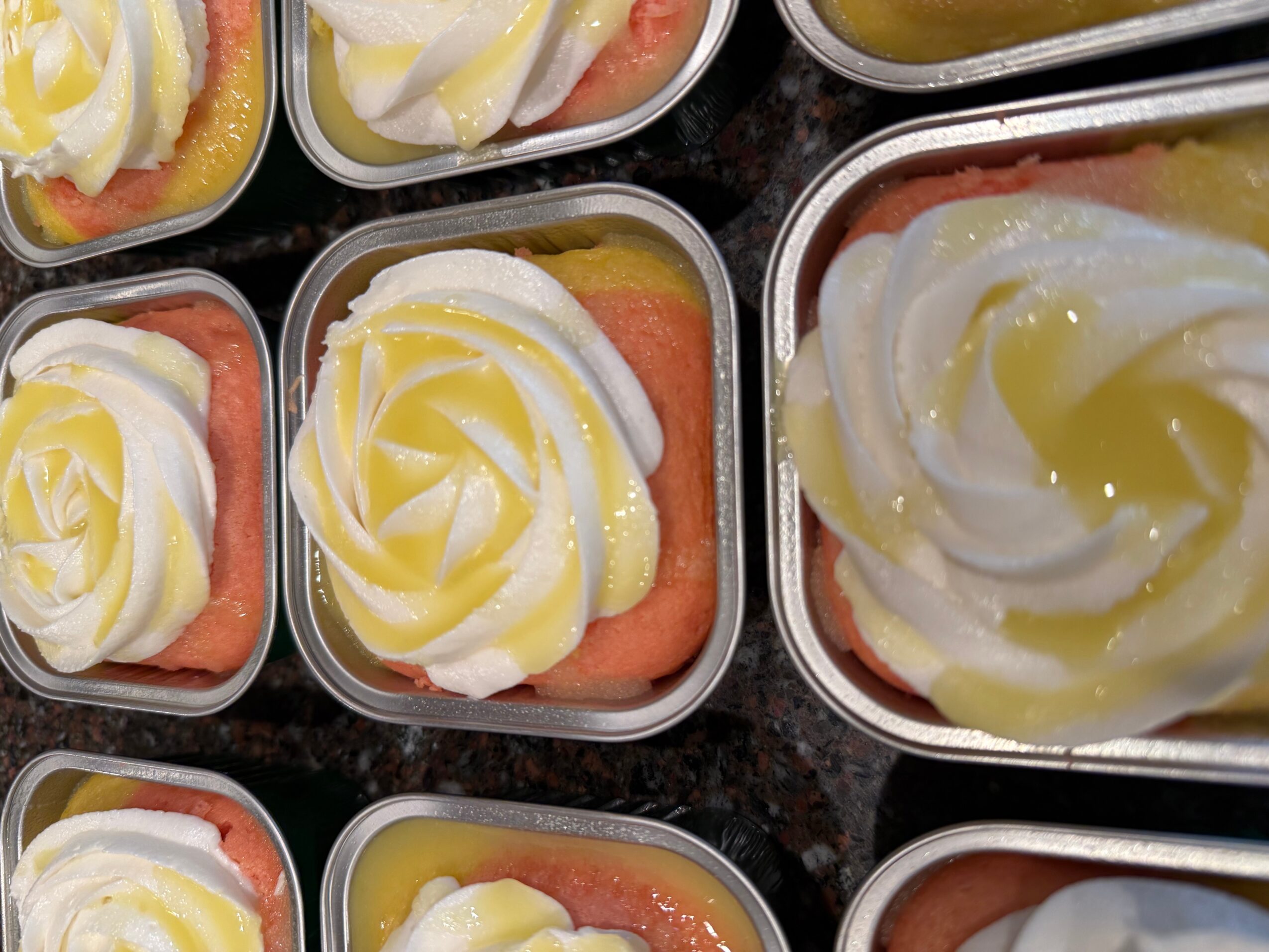 Multiple containers of watermelon topped with whipped cream and lemon zest, arranged on a dark surface.