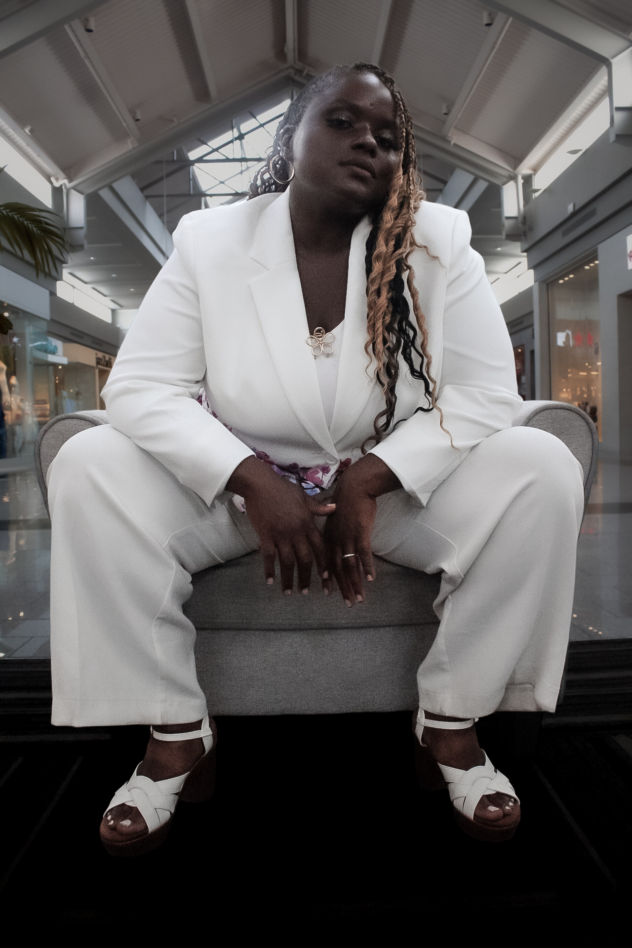 Person in a white suit sitting with legs apart in an indoor setting with high ceilings and glass structures.