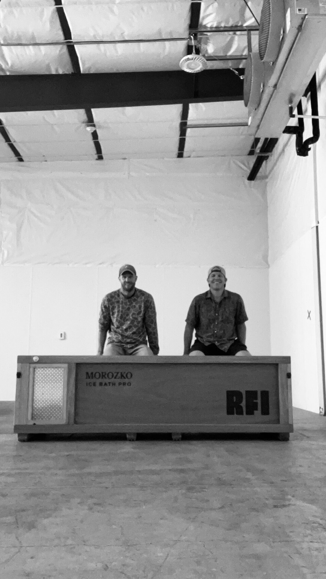Two people stand behind a desk in a large, industrial-style room with high ceilings and exposed pipes.