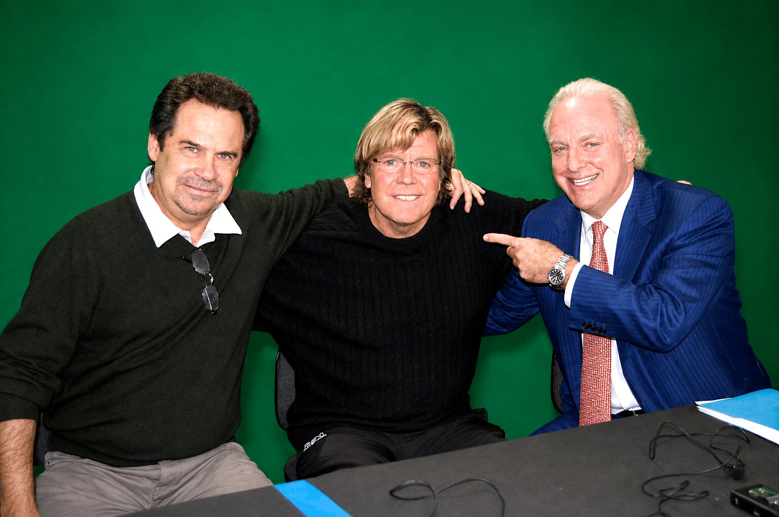 Three people sitting at a table with a green background, smiling and posing for the photo.
