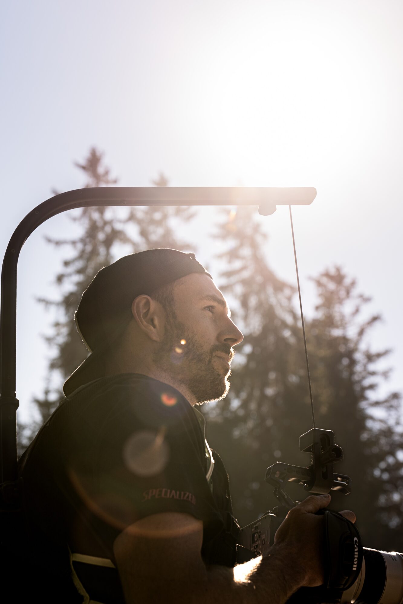 Silhouette of a man holding a camera outdoors with trees and bright sky in the background.